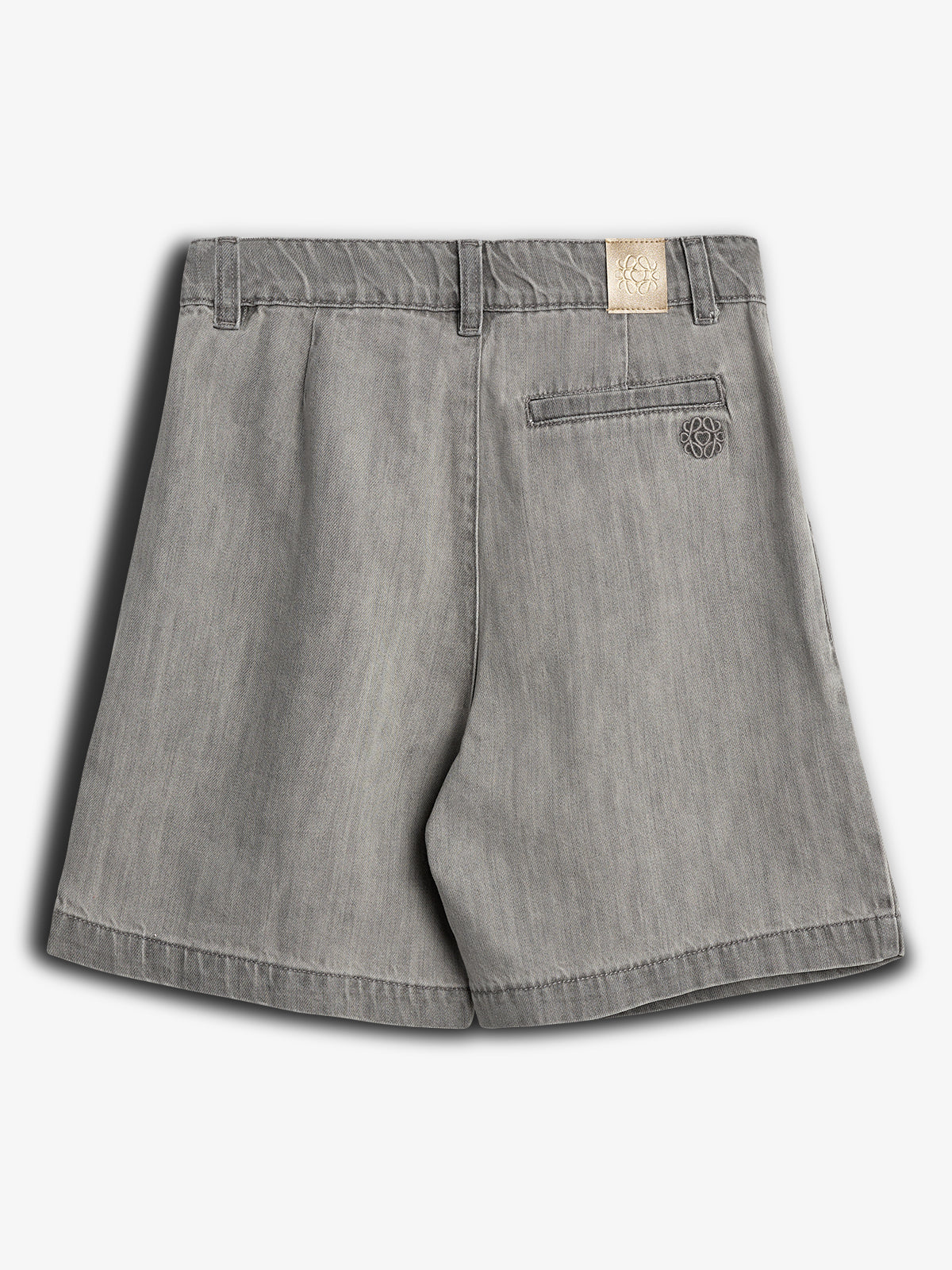 Een grijze korte broek ligt op een witte achtergrond. De broek heeft een achterzak en riemlussen, met een beige label en een geborduurd logo onder de zak.