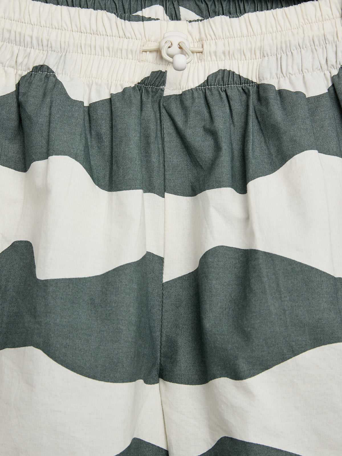Een elastische tailleband met een wit touwtje op een broek met brede grijze en witte horizontale strepen, gefotografeerd van dichtbij.