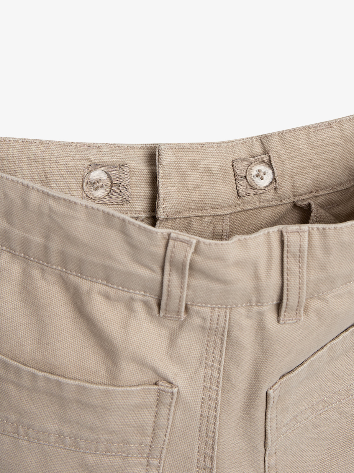 Beige pants lie flat, showing front buttons and belt loops, with visible front pockets and stitching details, against a plain white background.