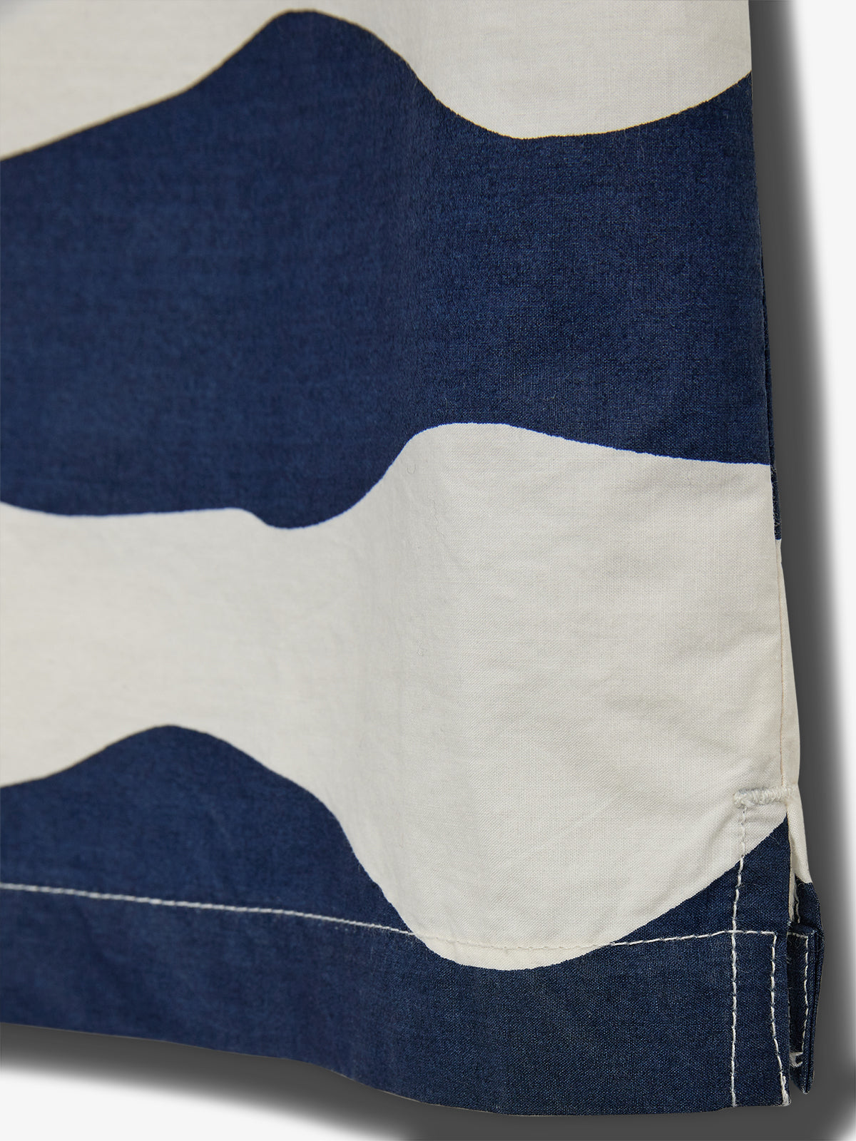 A piece of fabric features bold navy and white wavy stripes, stitched along the bottom edge, creating a seamless pattern. The fabric hangs vertically against a plain background.