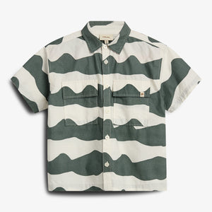 A short-sleeved button-up shirt features bold, wavy green and white stripes, with two front pockets. It is displayed against a plain white background.