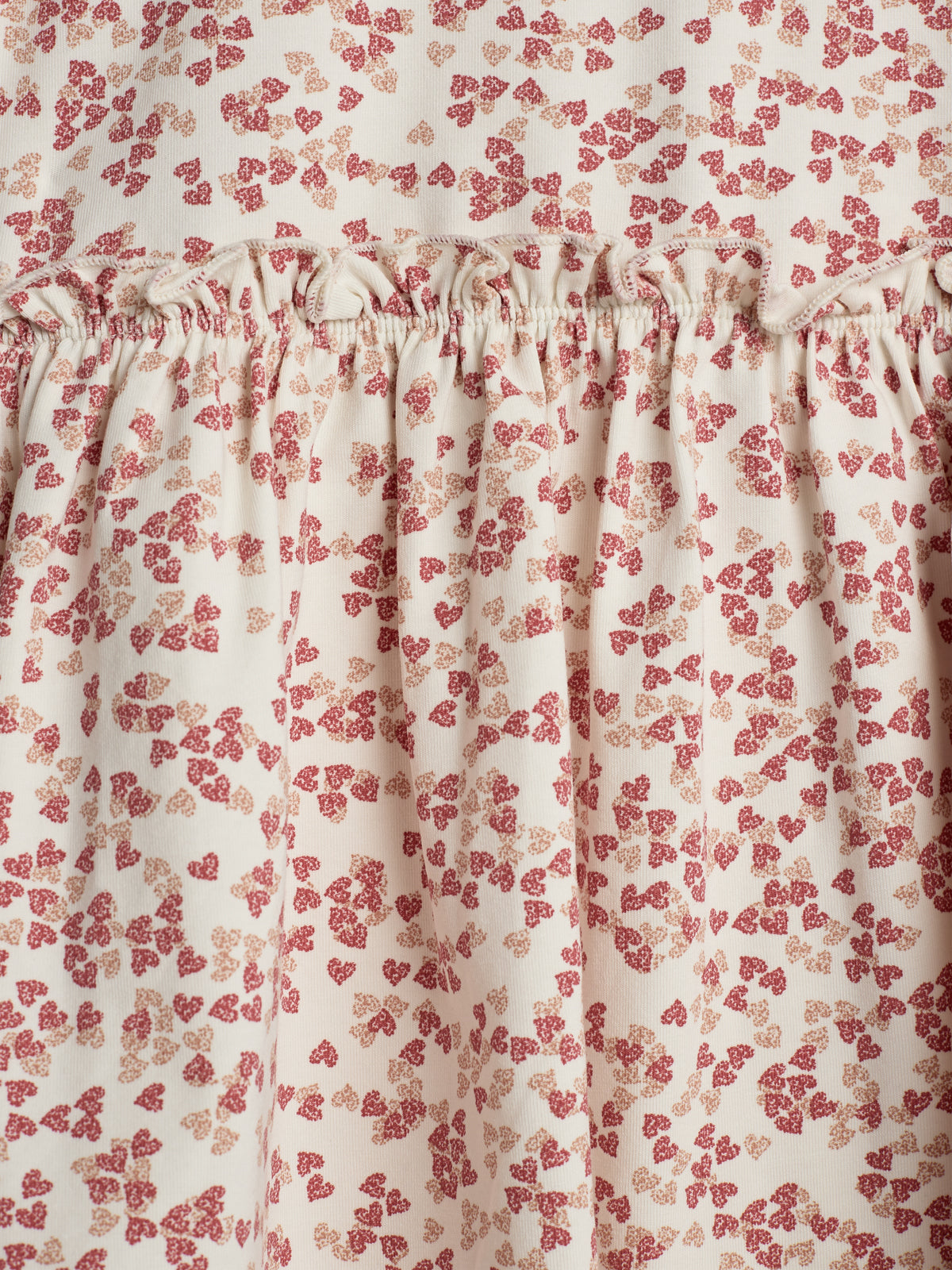 A cream-colored fabric with small red and beige floral patterns is gathered and sewn, creating a ruffled texture in a close-up view.