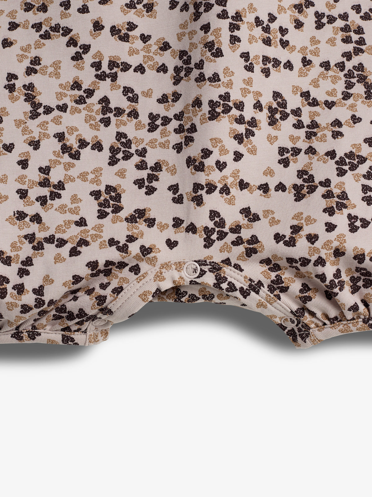 Stof met bruine en beige bloemenpatroon, liggend op een witte achtergrond. De stof heeft drukknopen aan de onderkant, suggereert gebruik in kleding zoals een babyromper.