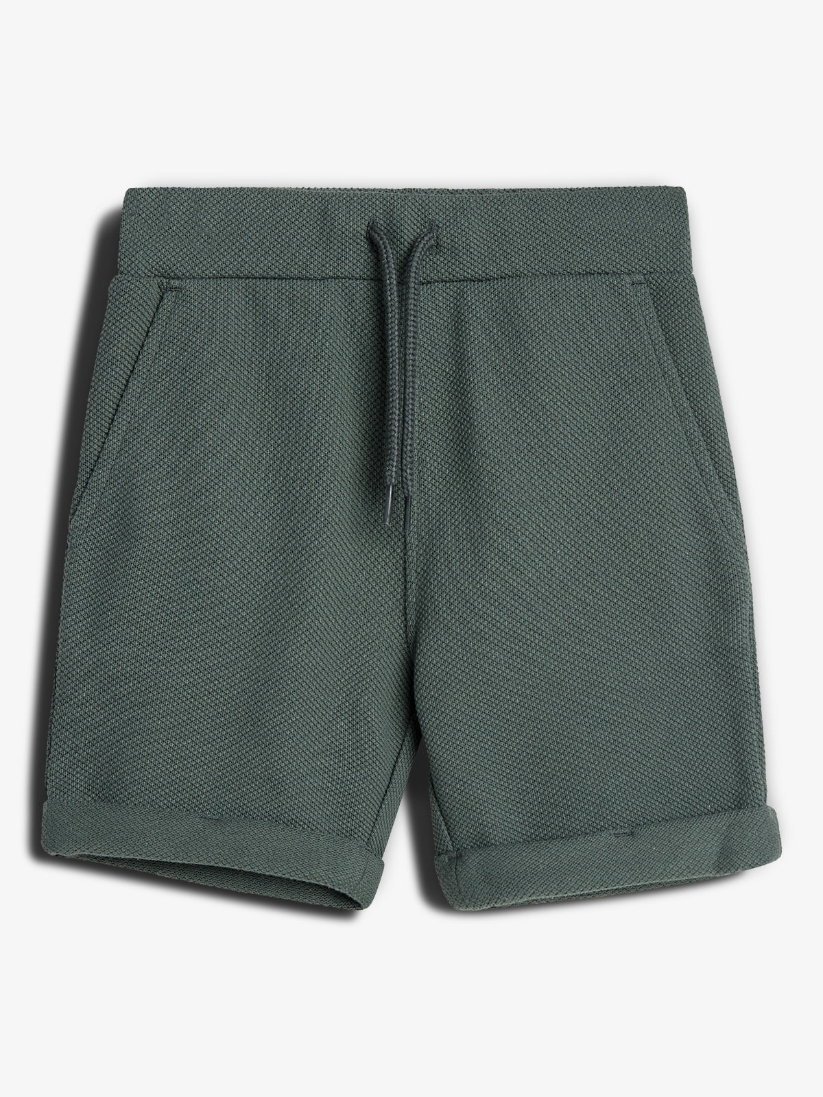 Een groene, textuur korte broek met omgeslagen pijpen en een trekkoord, ligt plat in een eenvoudige, neutrale omgeving.