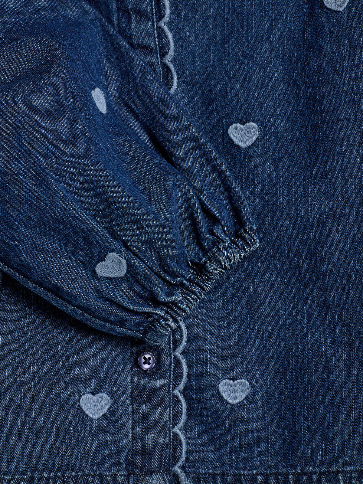 Denimstof met witte hartjes, een ingestikte mouw met elastische pols en een knoopsluiting met decoratieve rand.