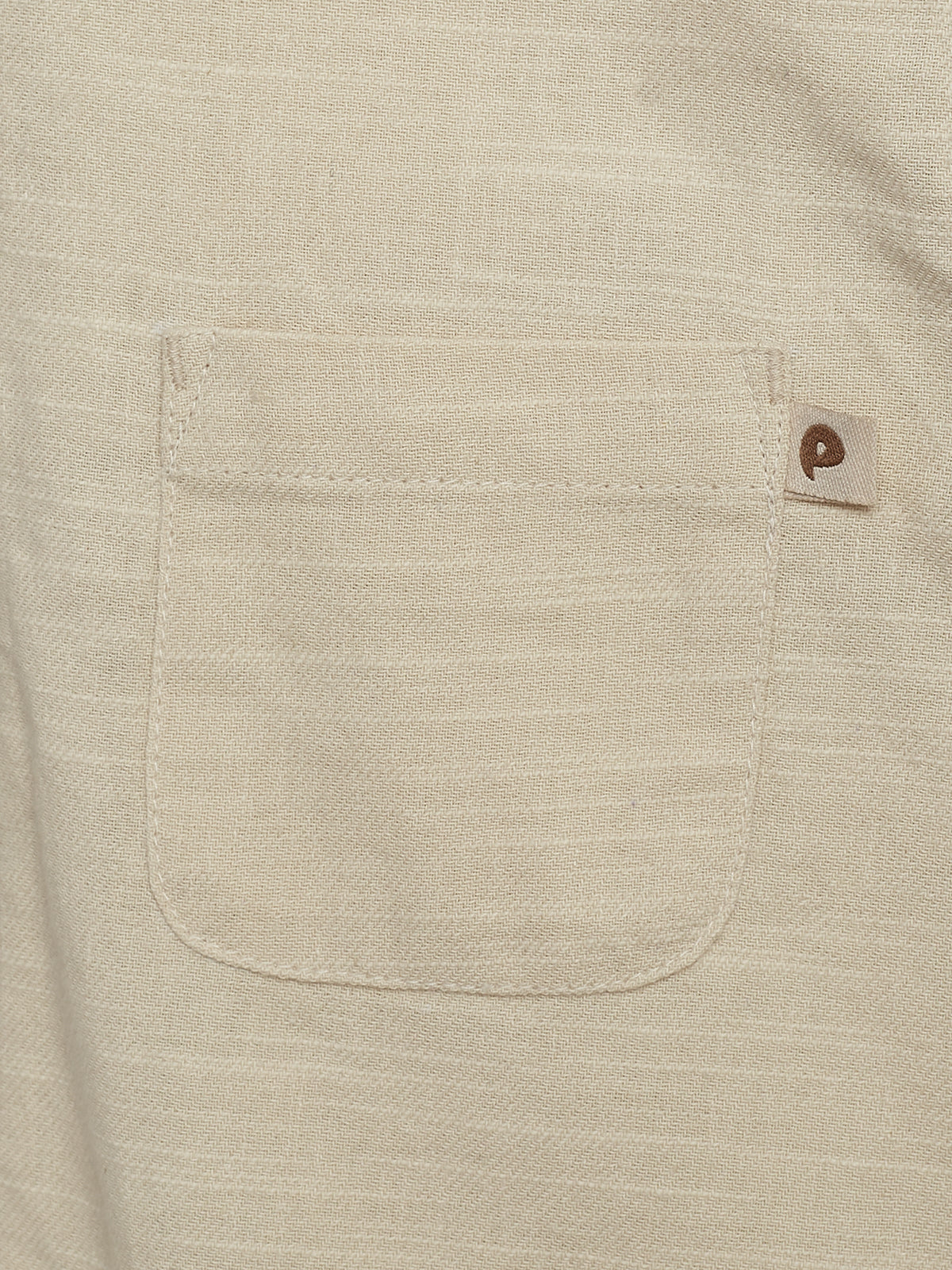 Een beige stoffen zak is genaaid op een kledingstuk. Er zit een klein labeltje met een logo in de rechterbovenhoek. De achtergrond is gelijkmatig en effen van kleur.