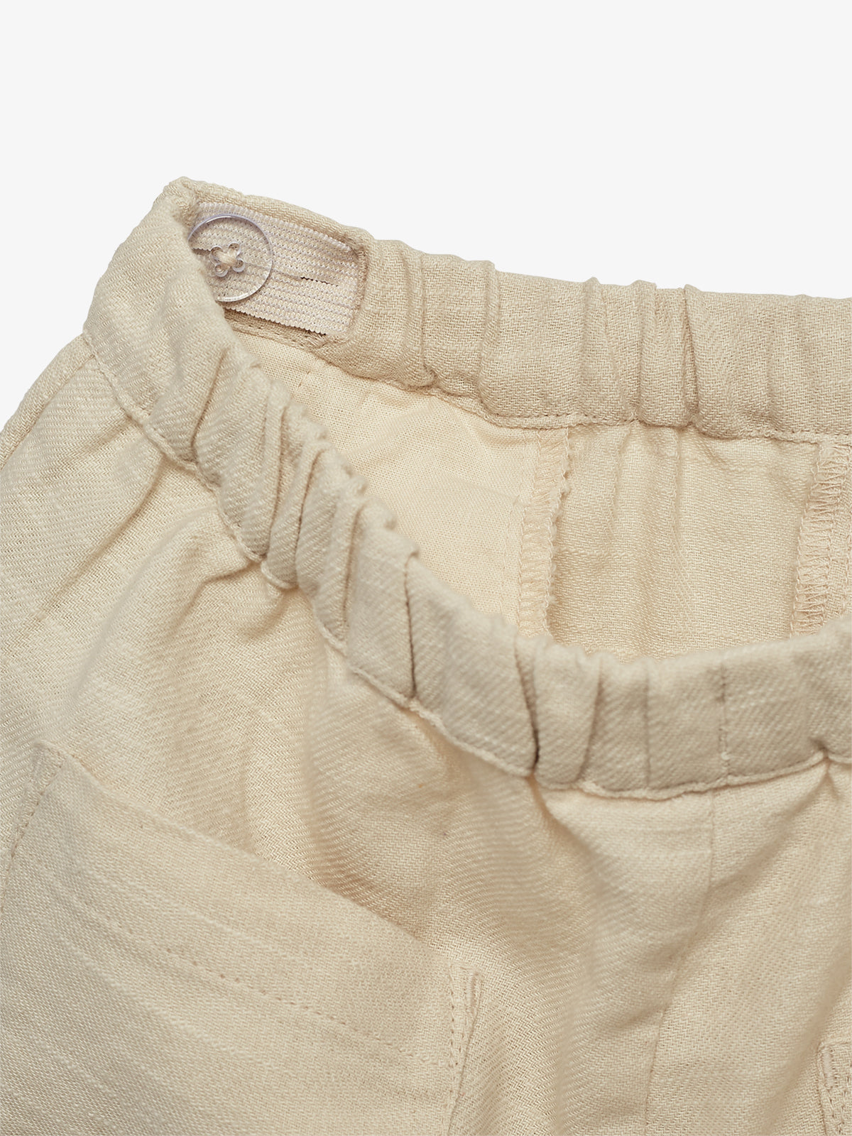 Beige broek met elastische tailleband en een knoop, zonder zichtbare tekst, gefotografeerd tegen een neutrale achtergrond.