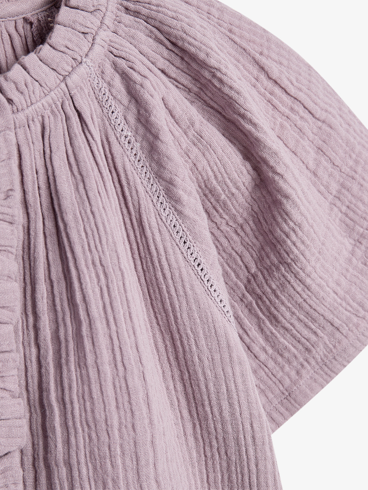 A light purple, textured fabric with vertical pleats forms a garment's shoulder section, detailed with decorative stitching, set against a plain white background.