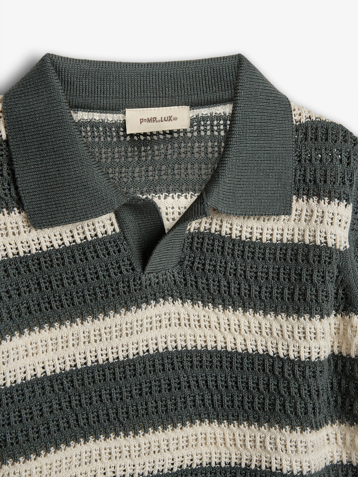 A knit polo shirt with alternating dark grey and cream stripes, featuring a ribbed collar. The label reads "poMP de LUX©," placed in a well-lit, white background.