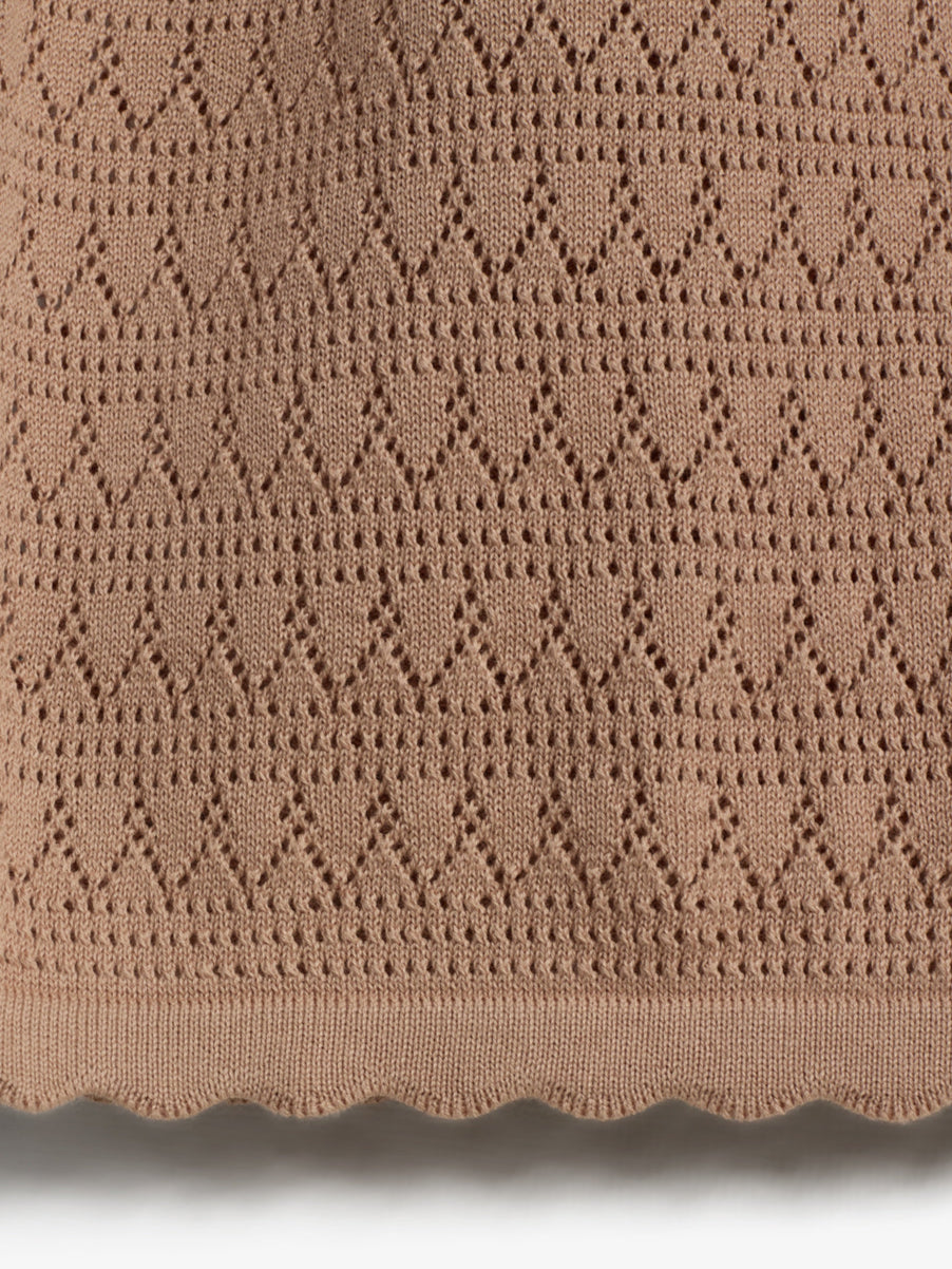 Beige fabric with diamond-patterned knit design, featuring small, evenly spaced holes and scalloped edges, set against a neutral background.