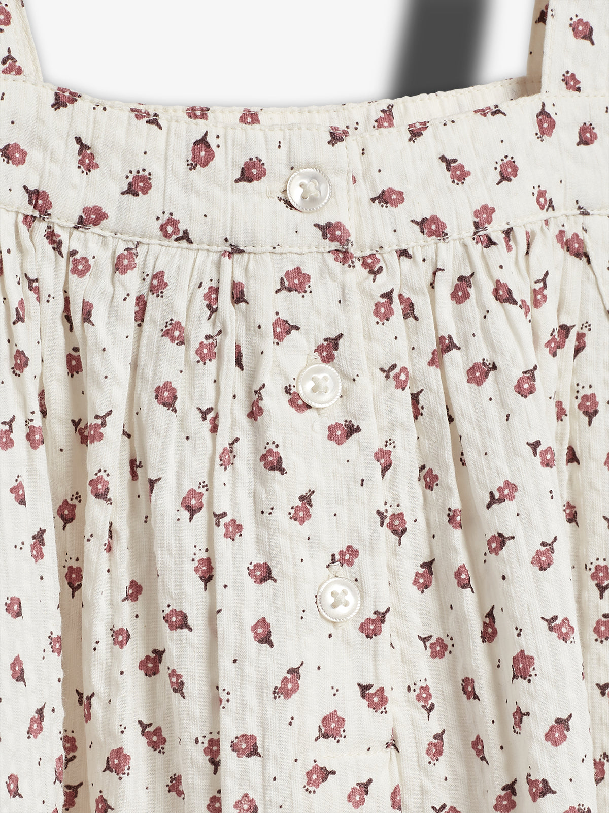 A cream-colored fabric with small red floral patterns features three white buttons down the center. The material appears gathered, suggesting a dress or skirt design.