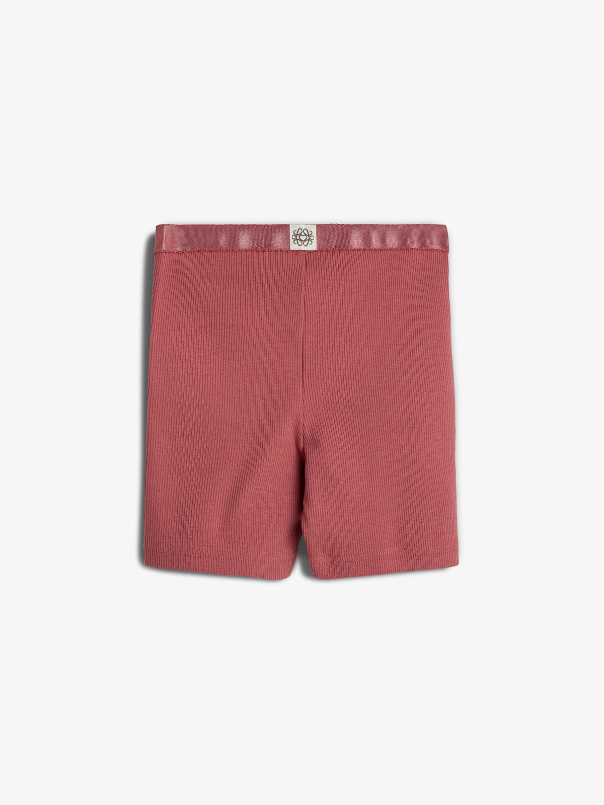 Red ribbed shorts lie flat, displaying a simple design with an elastic waistband against a plain white background. A small tag with a floral logo is attached to the waistband.