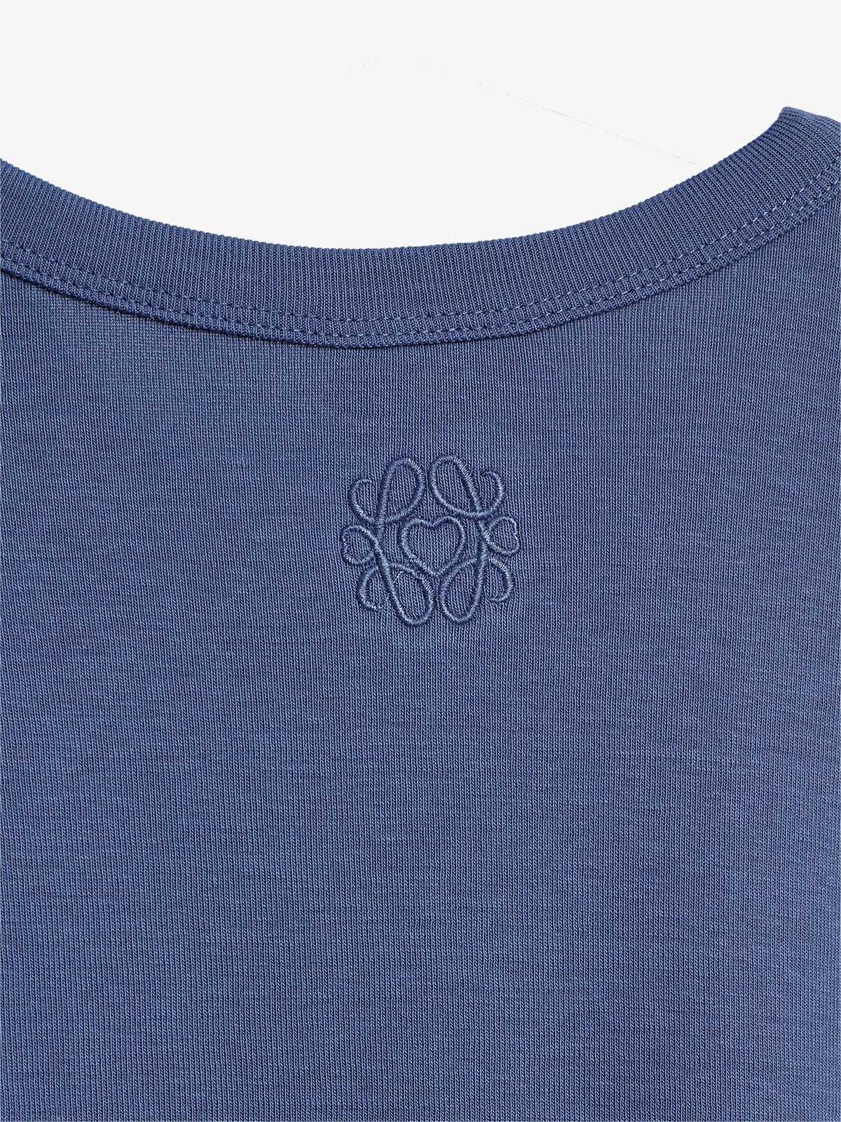 Blue shirt displays an embroidered intricate logo on the upper back, featuring looped and symmetrical designs, against a plain background.