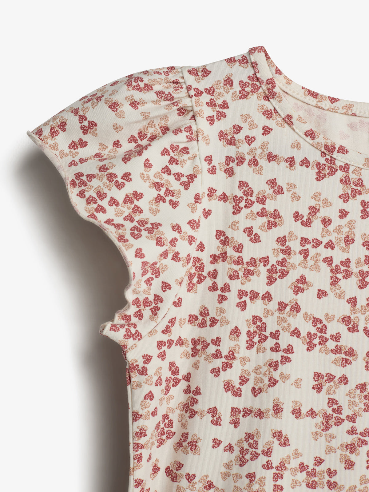A fabric with ruffled edges displays a pattern of small red and orange floral shapes, set against a plain white background. The texture appears soft and slightly textured.