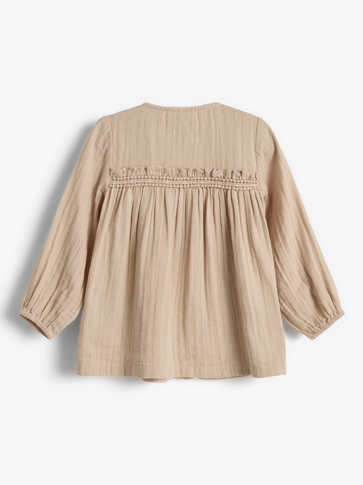 Beige blouse met lange mouwen hangt in een binnenruimte. De gerimpelde en geplooide details bovenaan geven een speels effect. Het materiaal oogt licht en geschikt voor dagelijks gebruik.