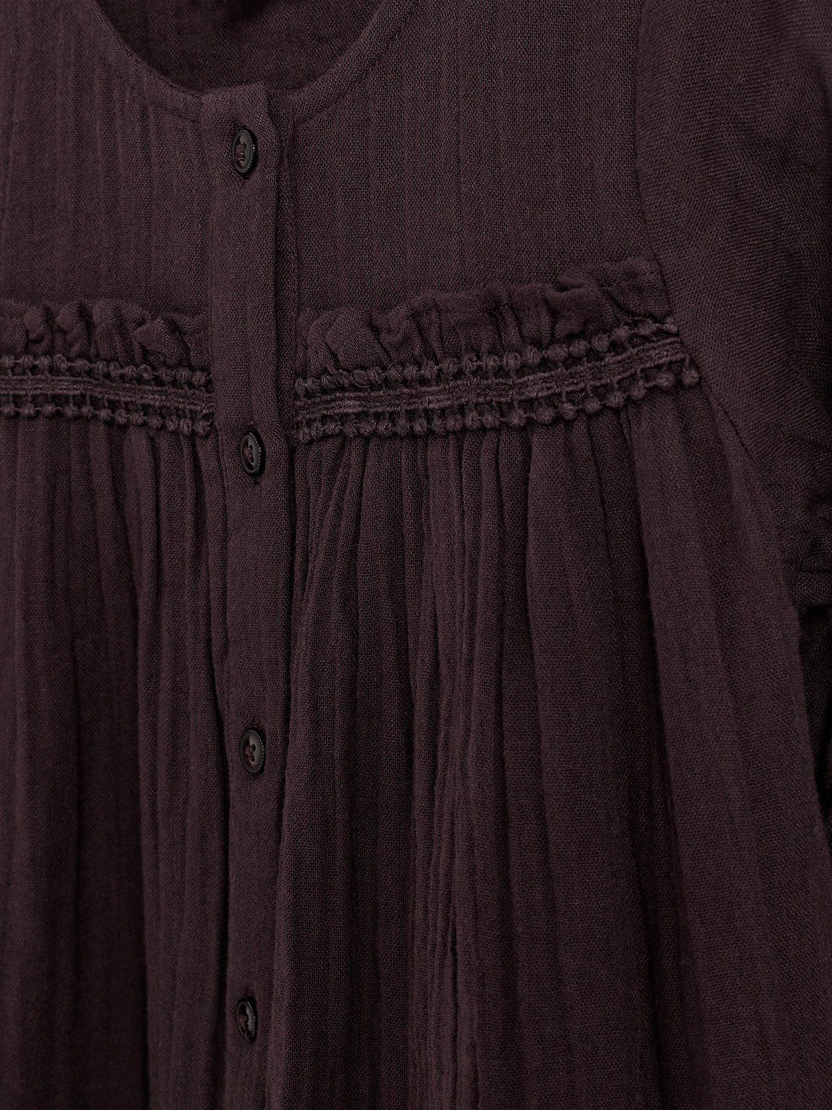 Een bruine, geplooide blouse met knoopsluiting aan de voorkant. De blouse heeft decoratieve stiksels en ruches, omgeven door een gelijkmatig getextureerde stof.