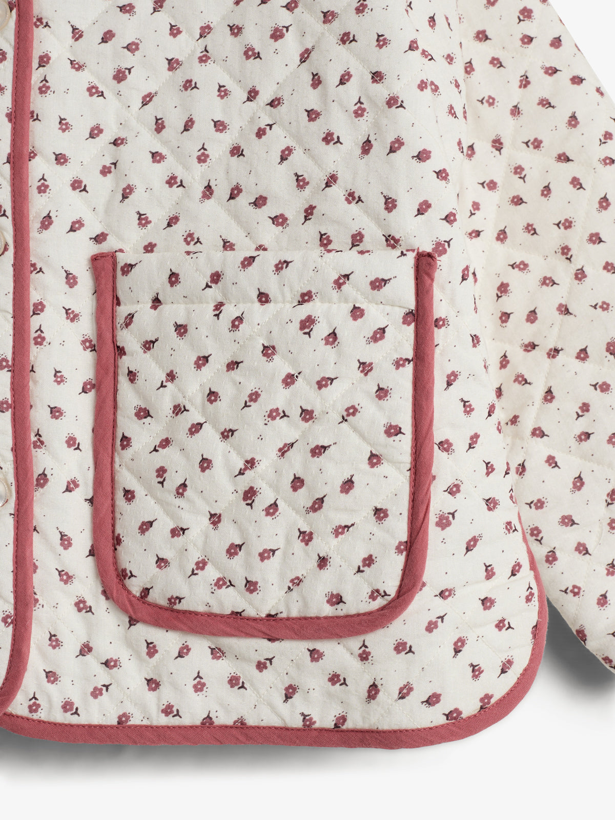 A quilted fabric with small pink floral patterns and a large pocket. It features pink piping along the edges, set against a plain white background.