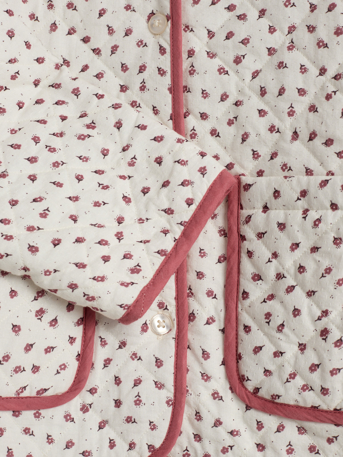 Quilted fabric with small pink floral pattern is stitched into a garment with pink trim and button detail. The fabric includes pockets, suggesting a cozy, feminine design.
