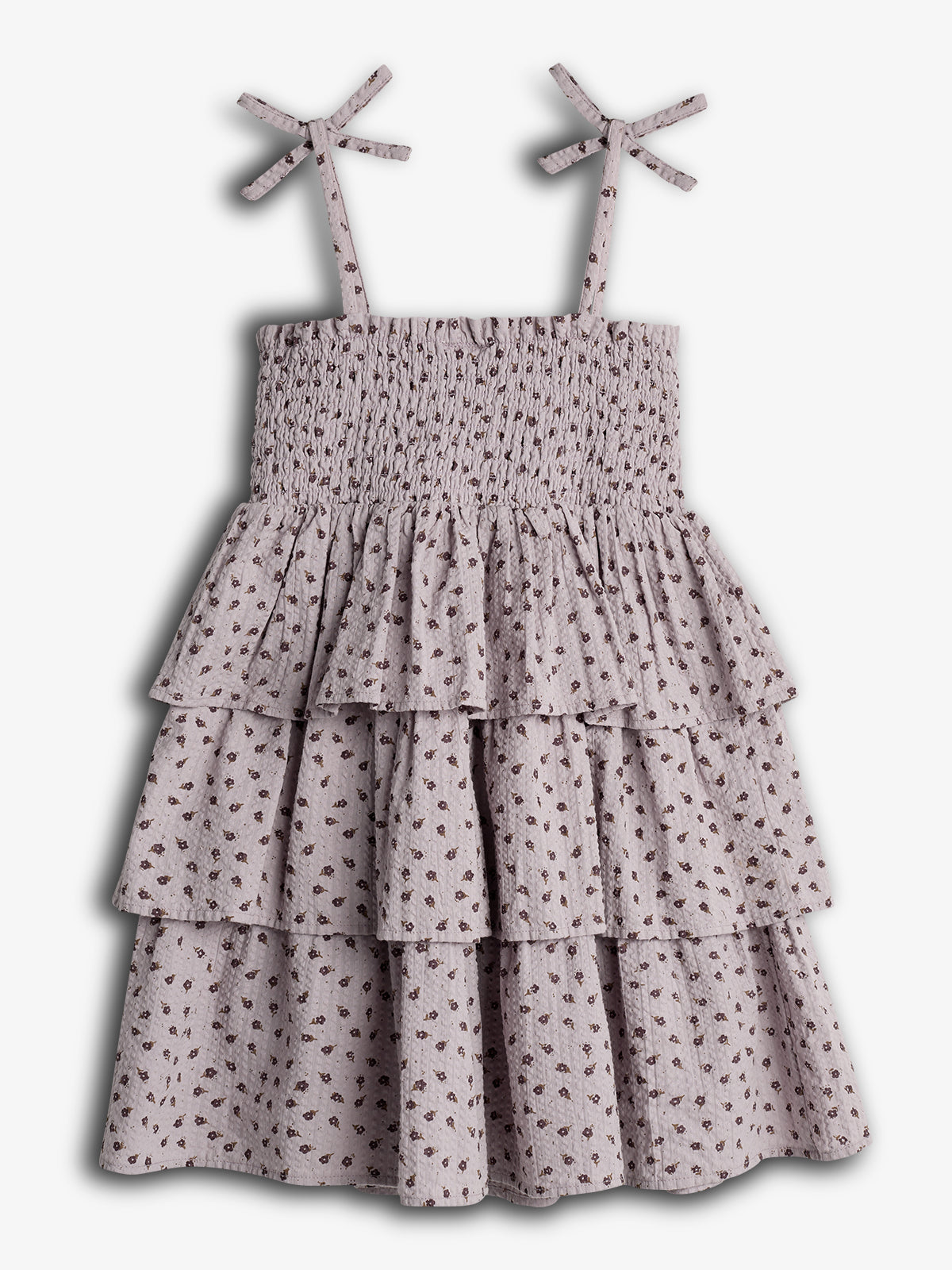 A sleeveless dress features tied shoulder straps and tiered ruffles. It's adorned with a small floral print and set against a plain, light background.