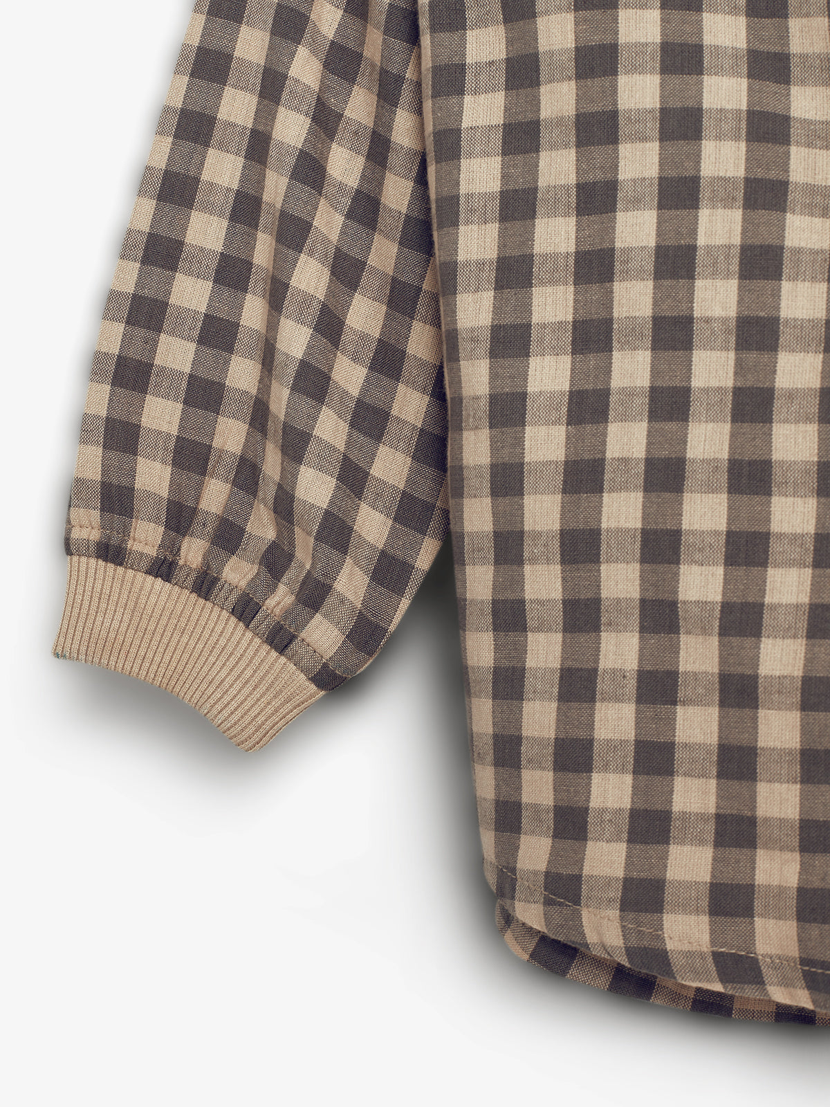 Een geruit kledingstuk met bruine en beige vierkanten, heeft een elastische manchetrand. Het hangt tegen een witte achtergrond.