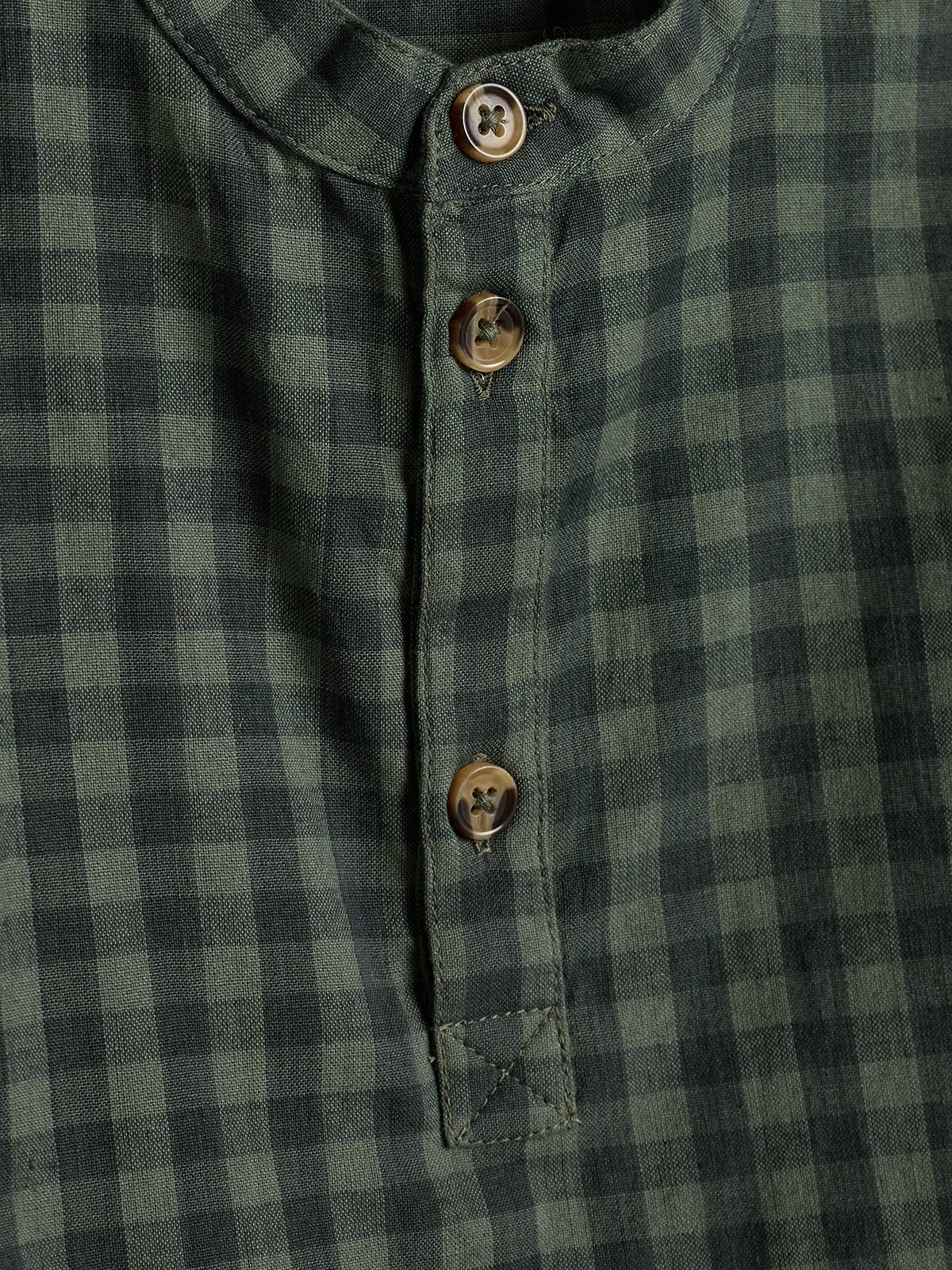 Een geruite blouse met groene en zwarte vierkanten, heeft drie bruine knopen aan de voorkant. De stof is geruit en de knopen zitten in een rechte lijn.