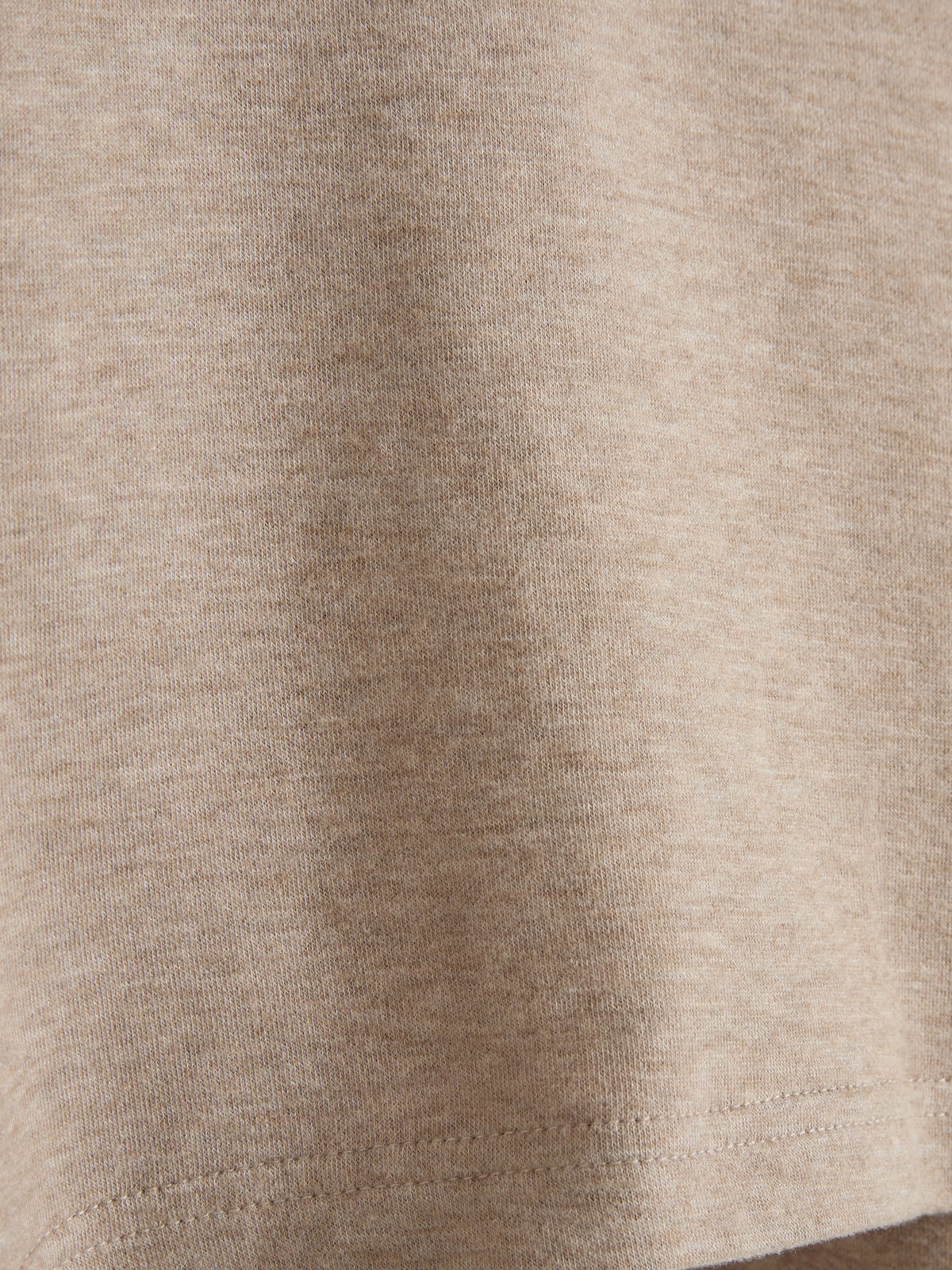 Een close-up van een beige T-shirtmateriaal, dat een gelijkmatige, fijngebreide textuur toont. Het bevindt zich tegen een eenvoudige achtergrond zonder zichtbare afleidingen of detail.