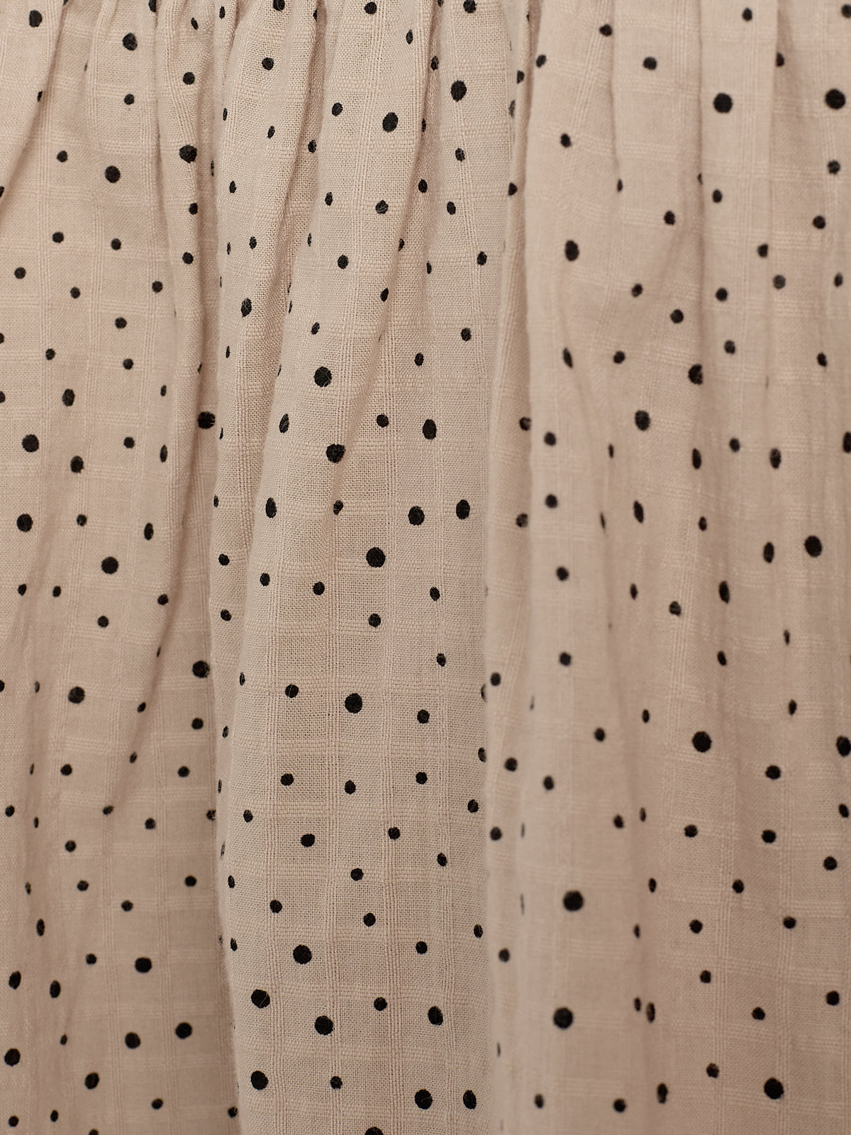 Beige fabric draped with black polka dots, creating a gathered texture across the surface.