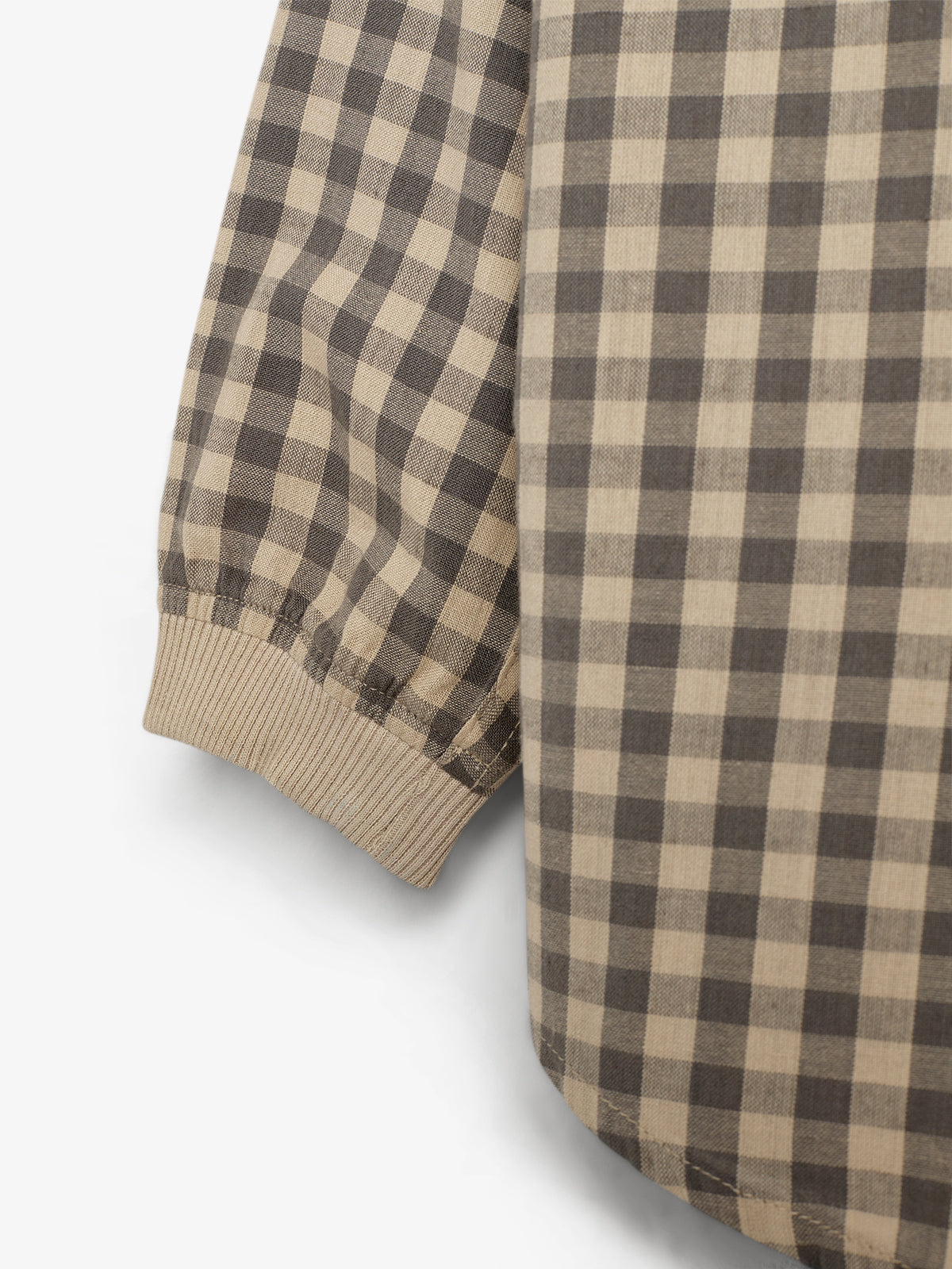 Een geruite mouw van een overhemd met beige en bruine vierkanten, eindigend in een elastische band, tegen een egale witte achtergrond.