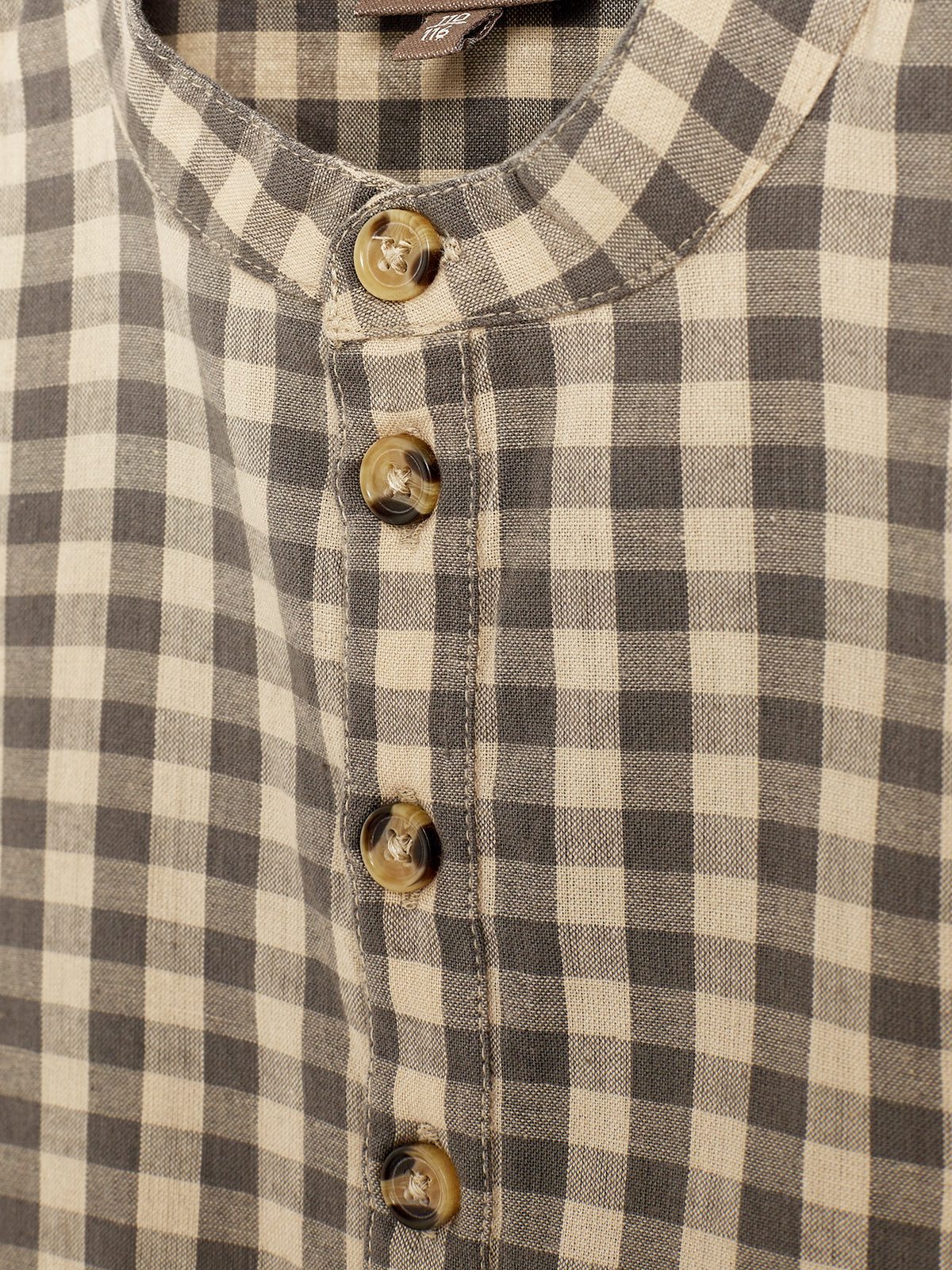 Een geruite blouse met bruine en beige vlakken, sluit met vijf beige knopen. De stof heeft een zachte textuur en de achtergrond is neutraal.