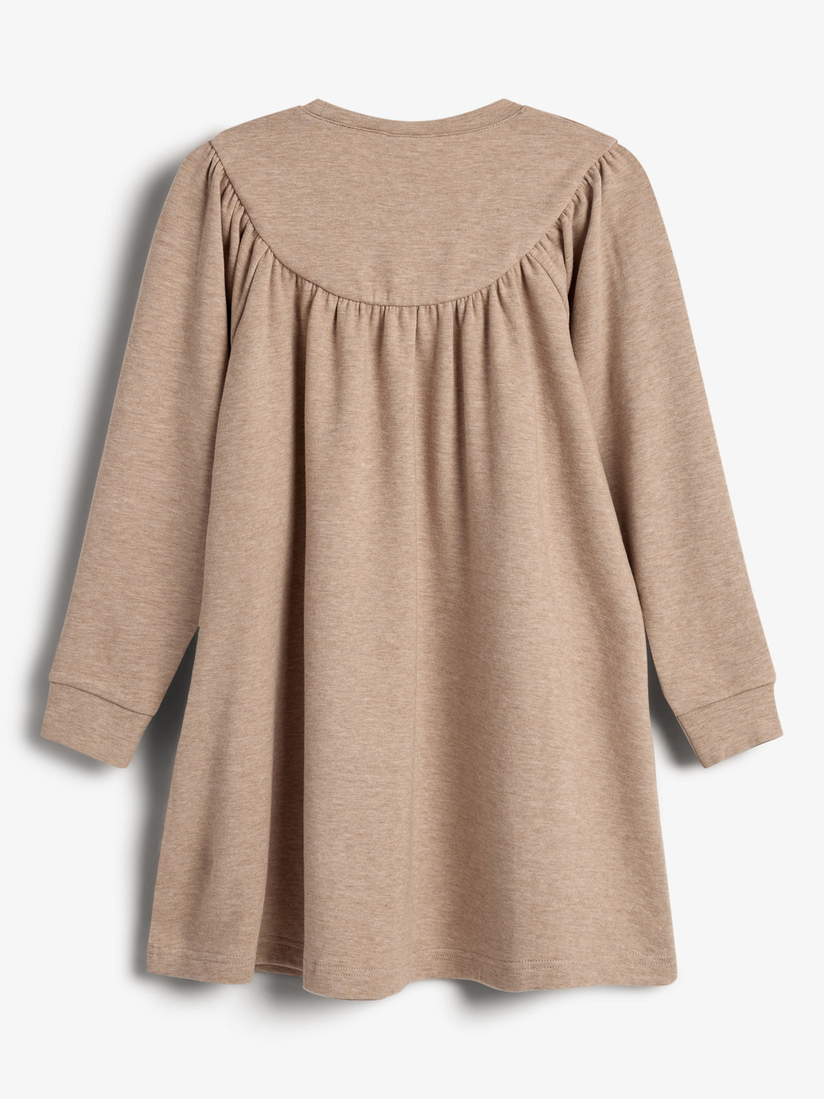 Een eenvoudige, beige jurk met lange mouwen hangt ongebruikt in een studioruimte tegen een witte achtergrond, gericht op de achterkant met geplooide details bij de schouders.