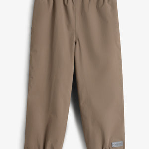 Een bruine regenbroek met elastische tailleband en enkels ligt plat. In de context van een lichte achtergrond. Rechtsonder is een grijs label te zien met de tekst: "Polarn O. Pyret."