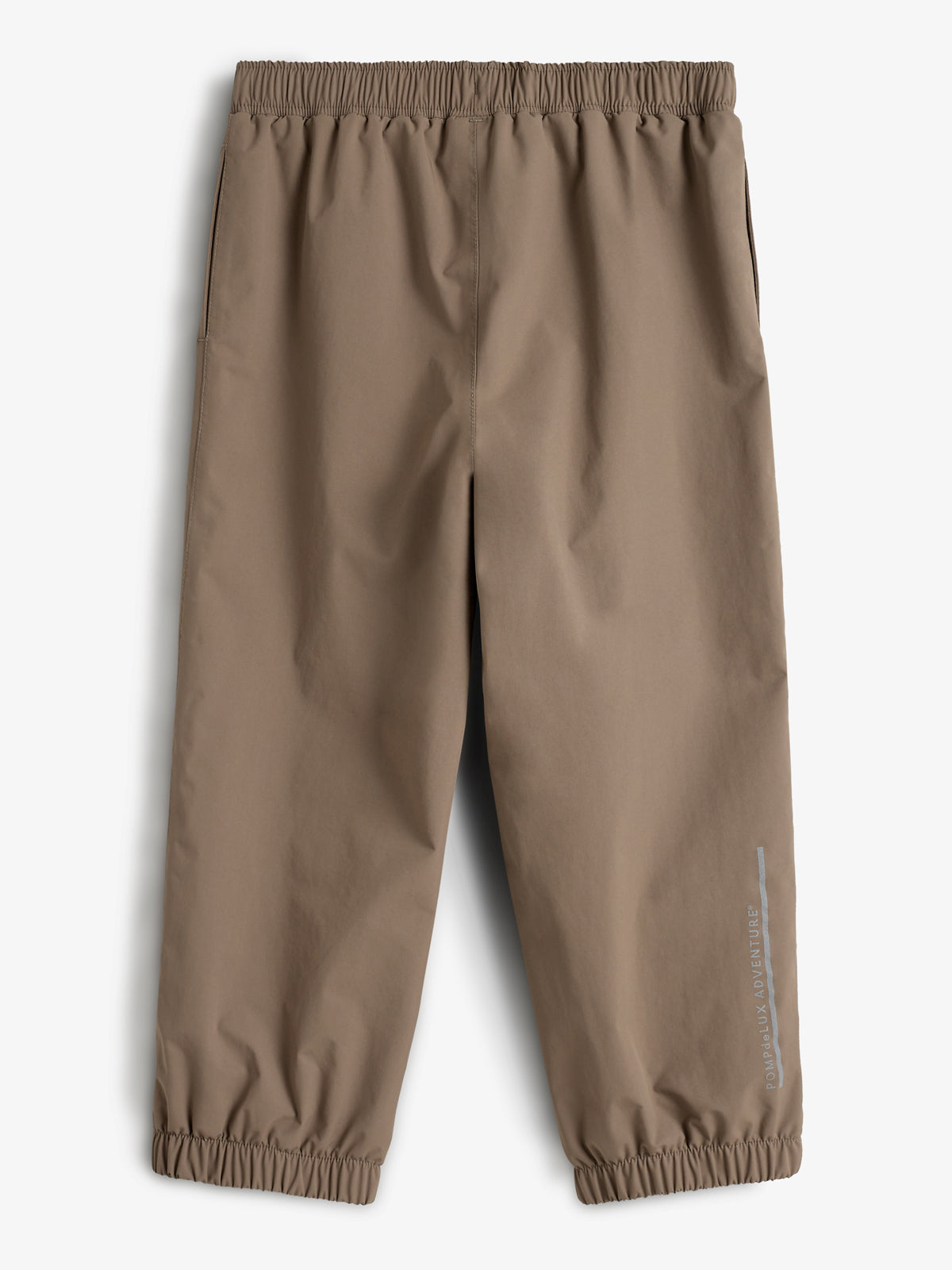 Bruine regenbroek met elastische taille en enkelbanden. De broek is in een minimalistische stijl. Tekst op de broek: "PO.PadkaLUX ADVENTURE". Geplaatst tegen een witte achtergrond.