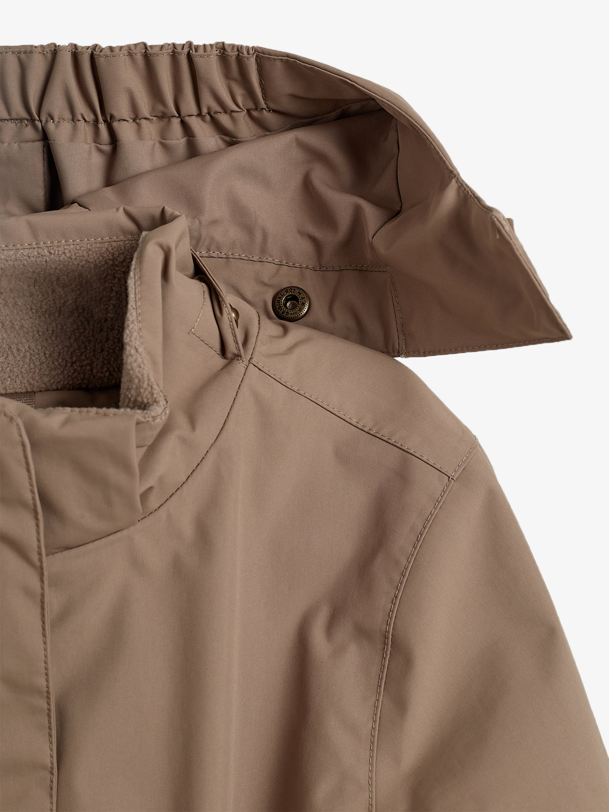 Een beige jas met een kraag en een knoop detail, ligt op een witte achtergrond. De jas heeft een elastisch randje aan de binnenkant van de kraag en zachte binnenkant.