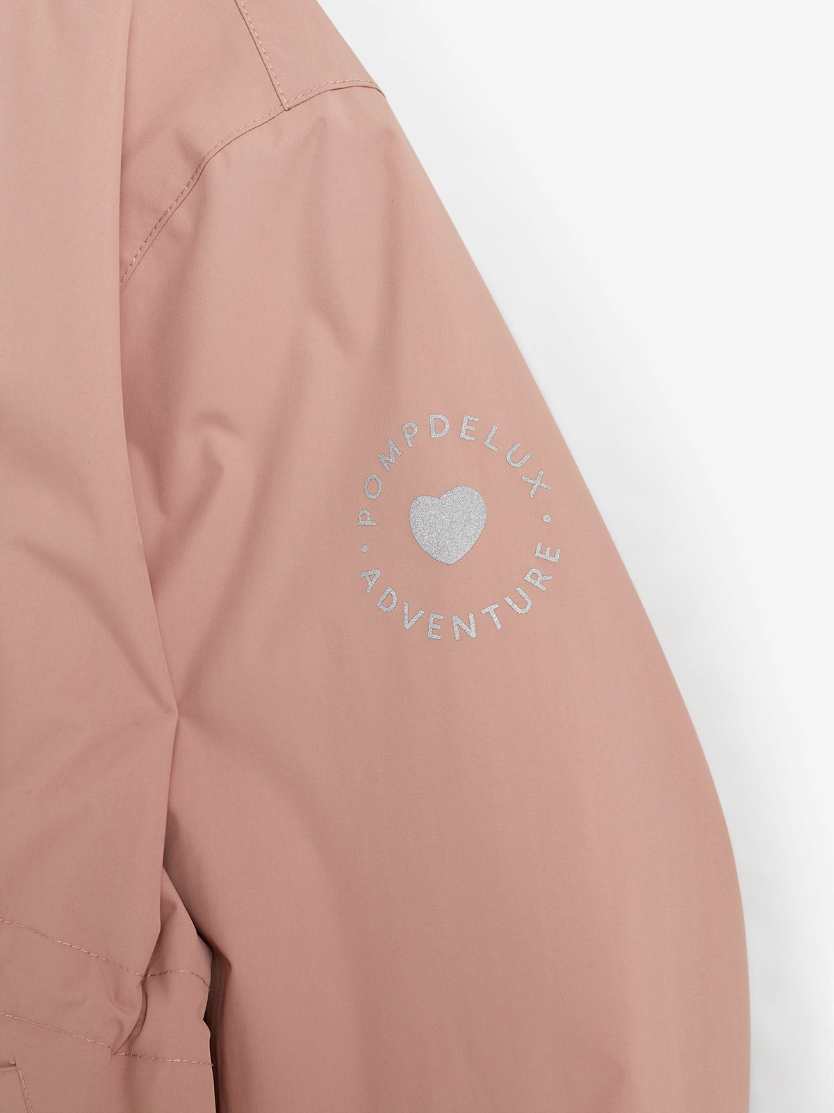Roze jas met tekst op de mouw: "POMPDELUX ADVENTURE" rondom een zilveren hartje. De achtergrond is wit.