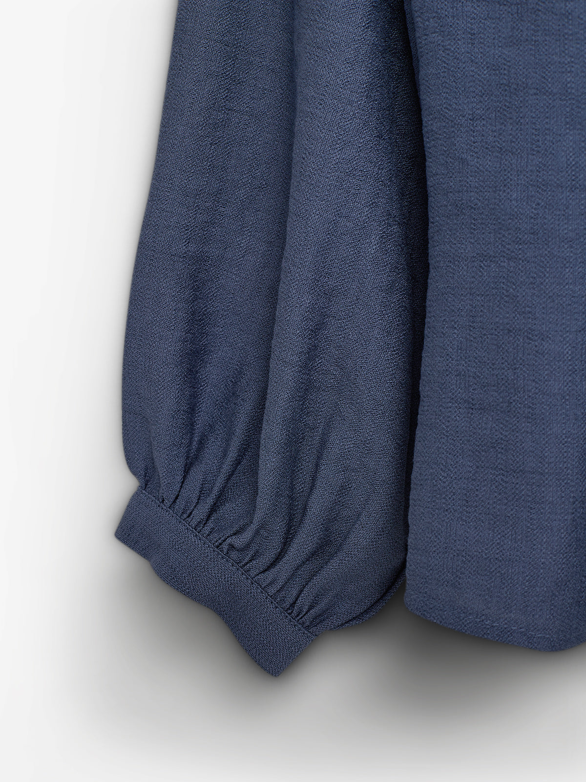 Een donkerblauwe mouw met elastische boorden hangt ontspannen tegen een egale, lichte achtergrond. De stof heeft een fijne textuur, die subtiel zichtbaar is.