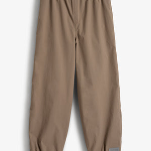 Een bruine broek hangt rechtop, met elastische tailleband en enkels. In een lichte, effen omgeving bevindt zich een label met de tekst "Polarn O. Pyret" rechtsonder.