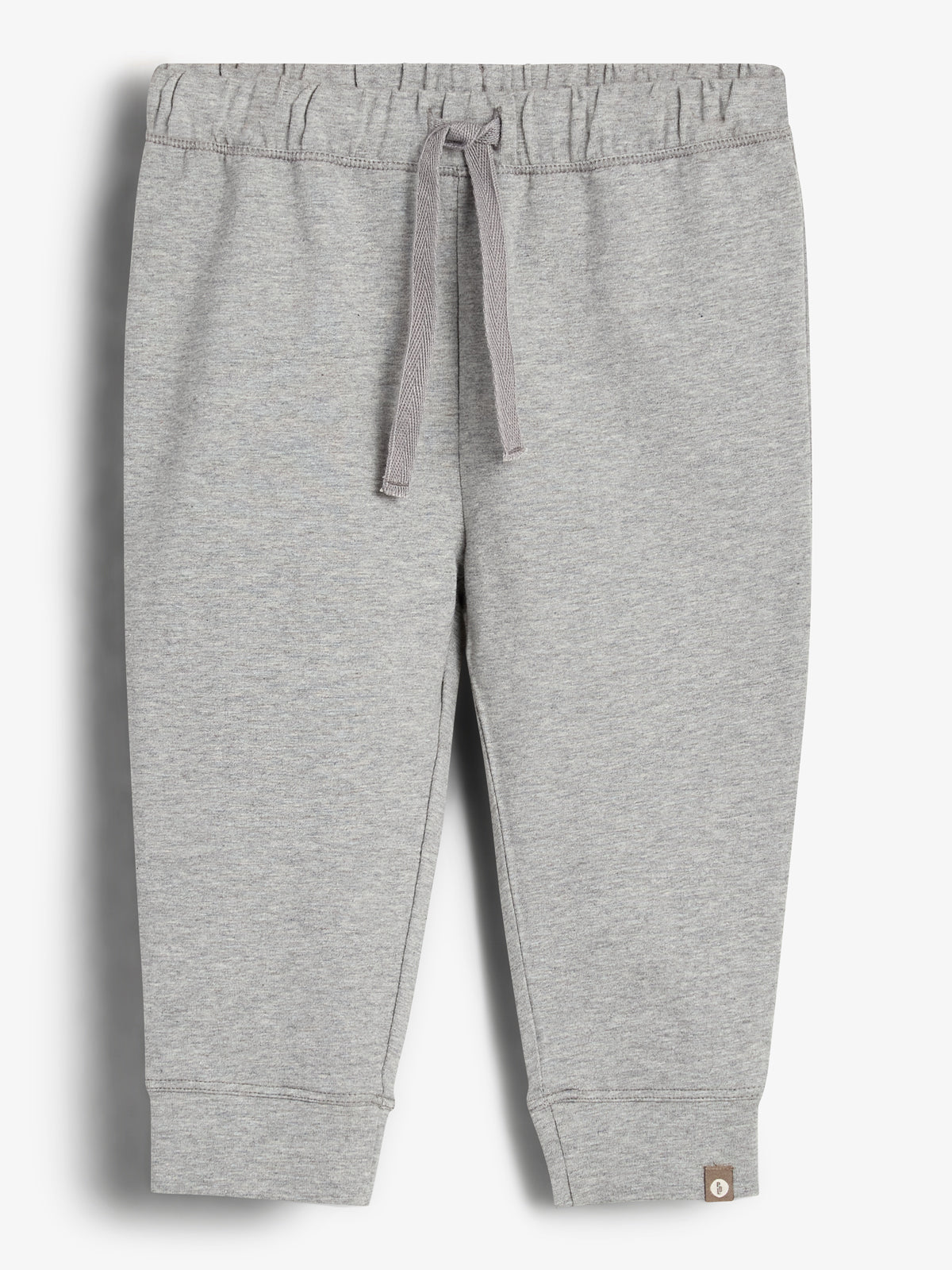 Grijze joggingbroek met een elastische tailleband en trekkoord. De broek heeft enkelboorden en een klein bruin label op de linkerpijp. De achtergrond is egaal wit.