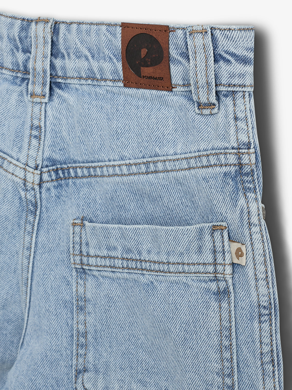 Een lichtblauwe spijkerbroek met een achterzak, voorzien van een bruine leren patch met een zwart "P"-logo en de tekst "POMPEBLUX", in een neutrale studio-omgeving.