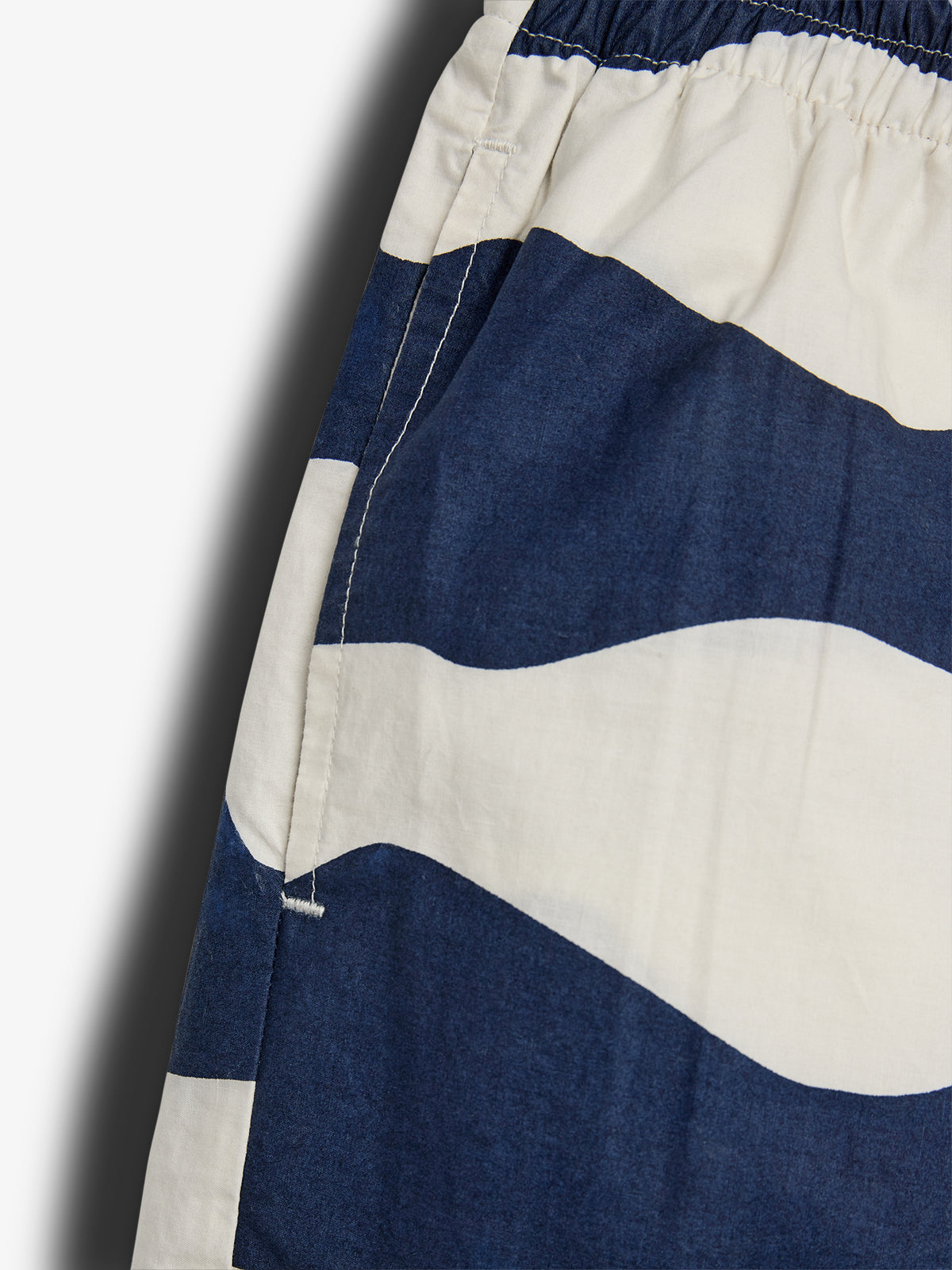Korte broek met blauw-wit golfpatroon, elastische tailleband zichtbaar. Gemaakt van een lichte stof, waarschijnlijk casual gelegenheden, gefotografeerd op een eenvoudige achtergrond.