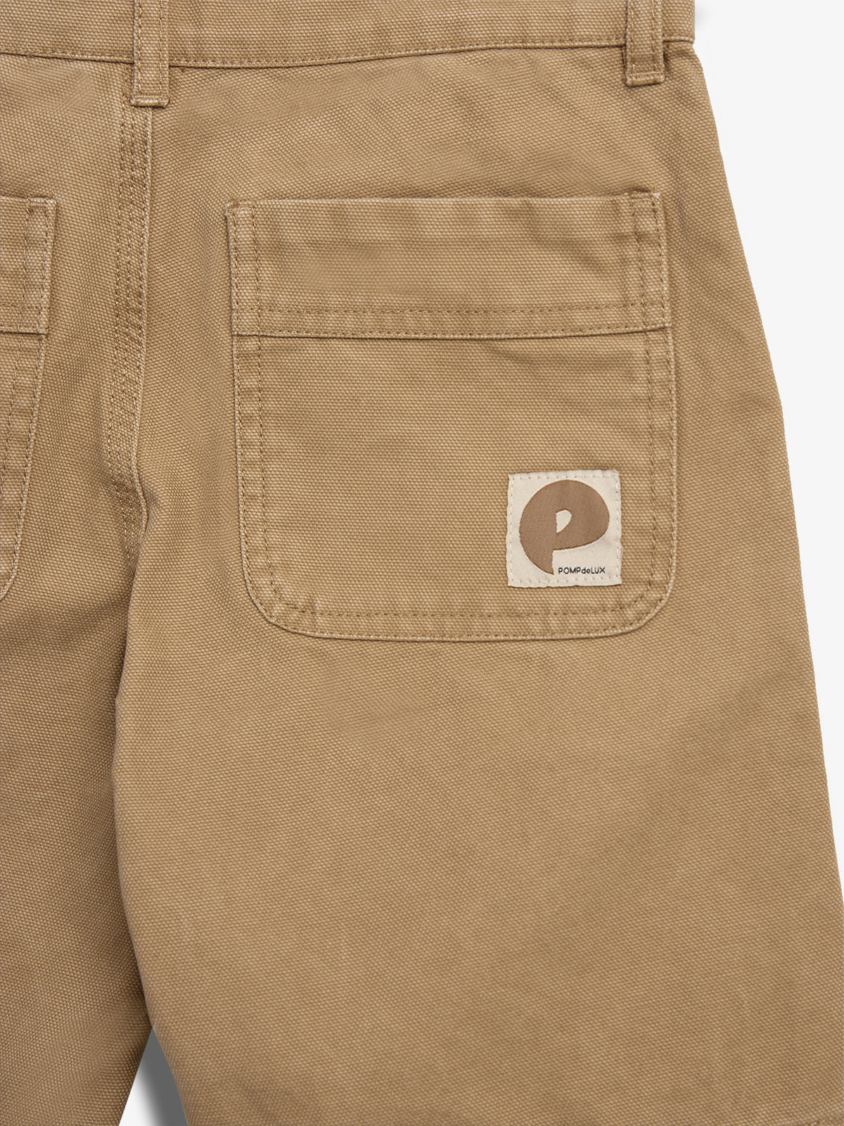 Een beige broekzak met een label met een bruin logo en de tekst "POW" en "POM POM" erop, is zichtbaar tegen een effen achtergrond.