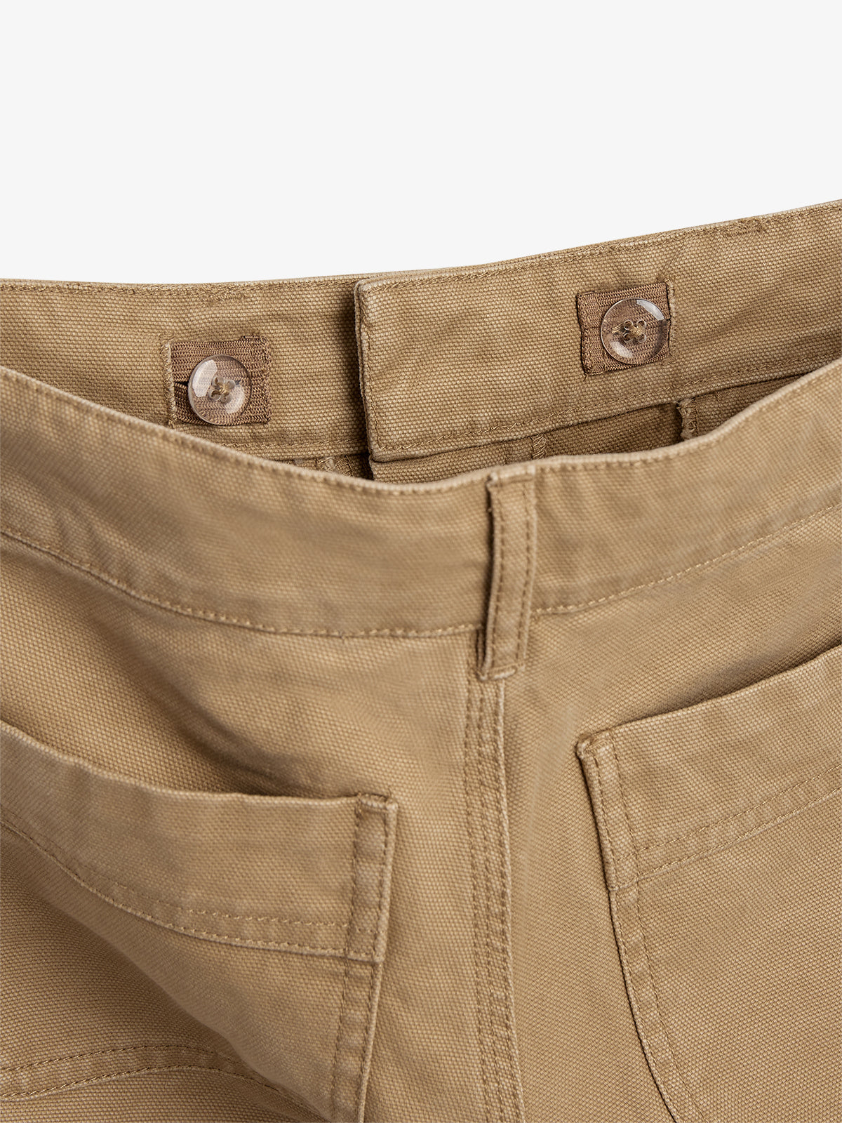 Een beige broek met een duidelijk zichtbare tailleband en twee knoppen. De zakken zijn zichtbaar aan de voorkant. De achtergrond is neutraal wit, zonder extra elementen.