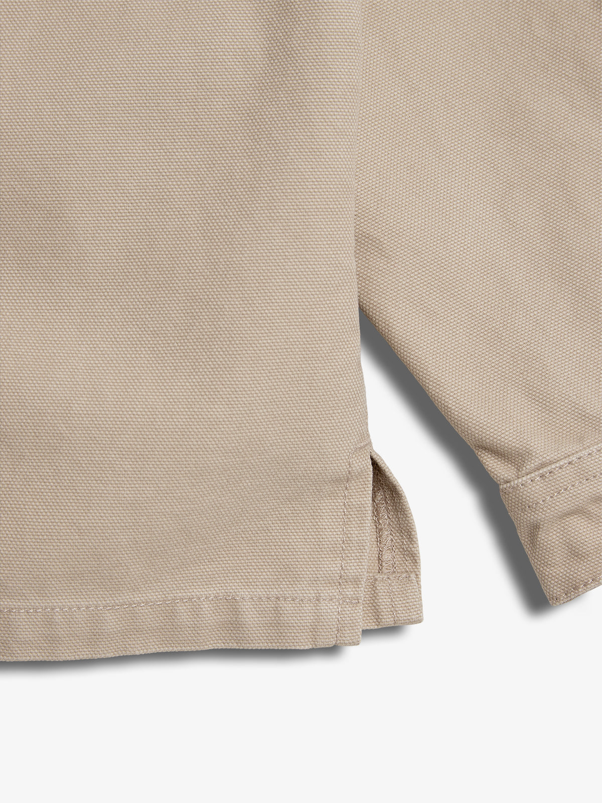 A close-up of a beige fabric with a textured weave, featuring a side slit and seam detail, lying flat on a surface.