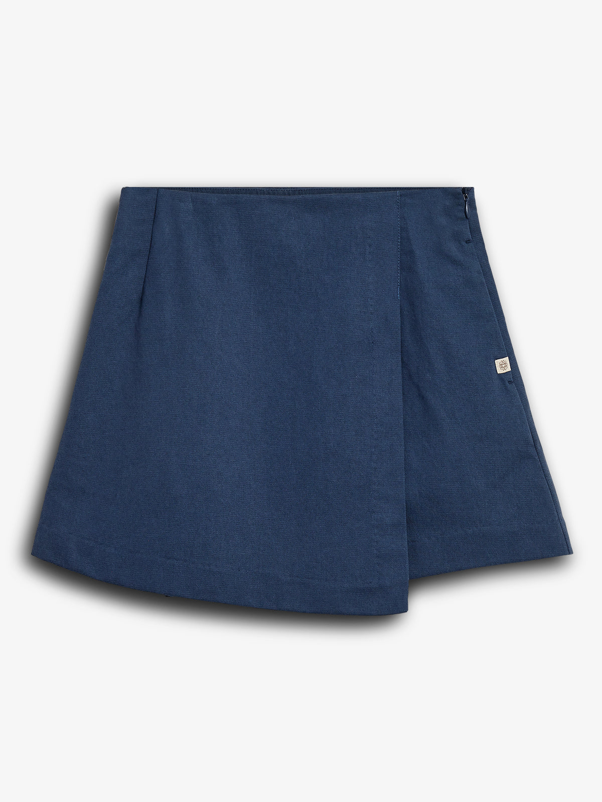 Een blauwe, korte rok hangt statisch tegen een witte achtergrond. De rok heeft een overlappende voorkant met subtiele stiksels en een klein merkje aan de zijkant.