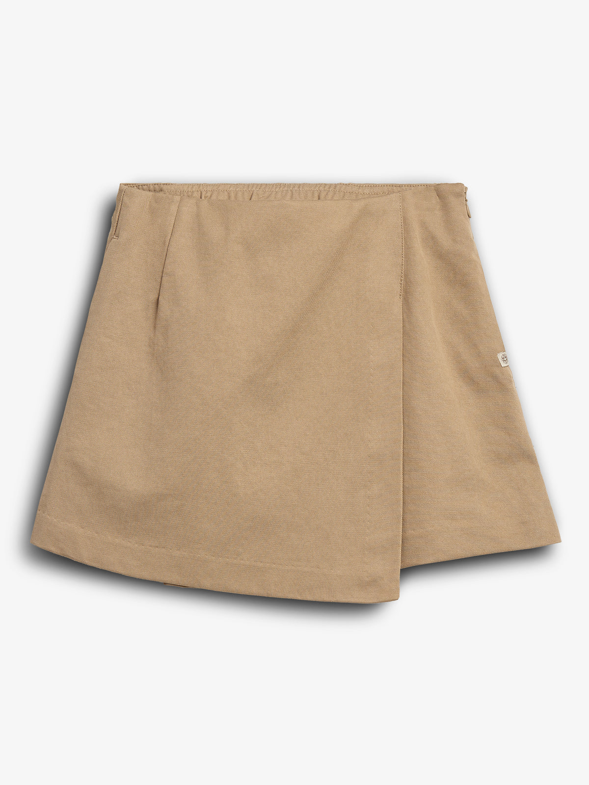 Een beige rok ligt plat, zonder versiering, met een subtiele plooi in het midden. De achtergrond is wit, en er is een klein label aan de zijkant.
