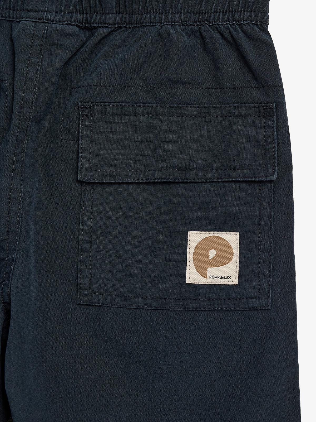 Donkere broek met een grote zak aan de rechterkant, voorzien van een bruin logo met de tekst "POMPdeLUX", in een neutrale achtergrond.