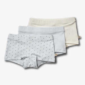 Drie stapels kindersonderbroeken; de voorste met blauwe stippen, de middelste effen lichtblauw, en de achterste crème met stippen, liggend op een witte achtergrond.