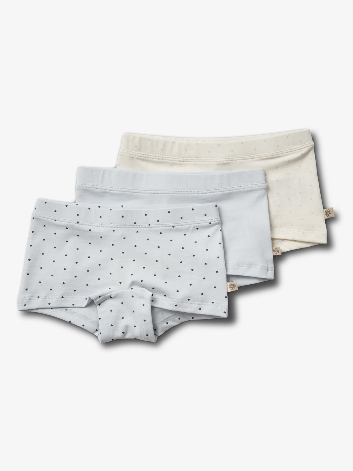 Drie stapels kindersonderbroeken; de voorste met blauwe stippen, de middelste effen lichtblauw, en de achterste crème met stippen, liggend op een witte achtergrond.
