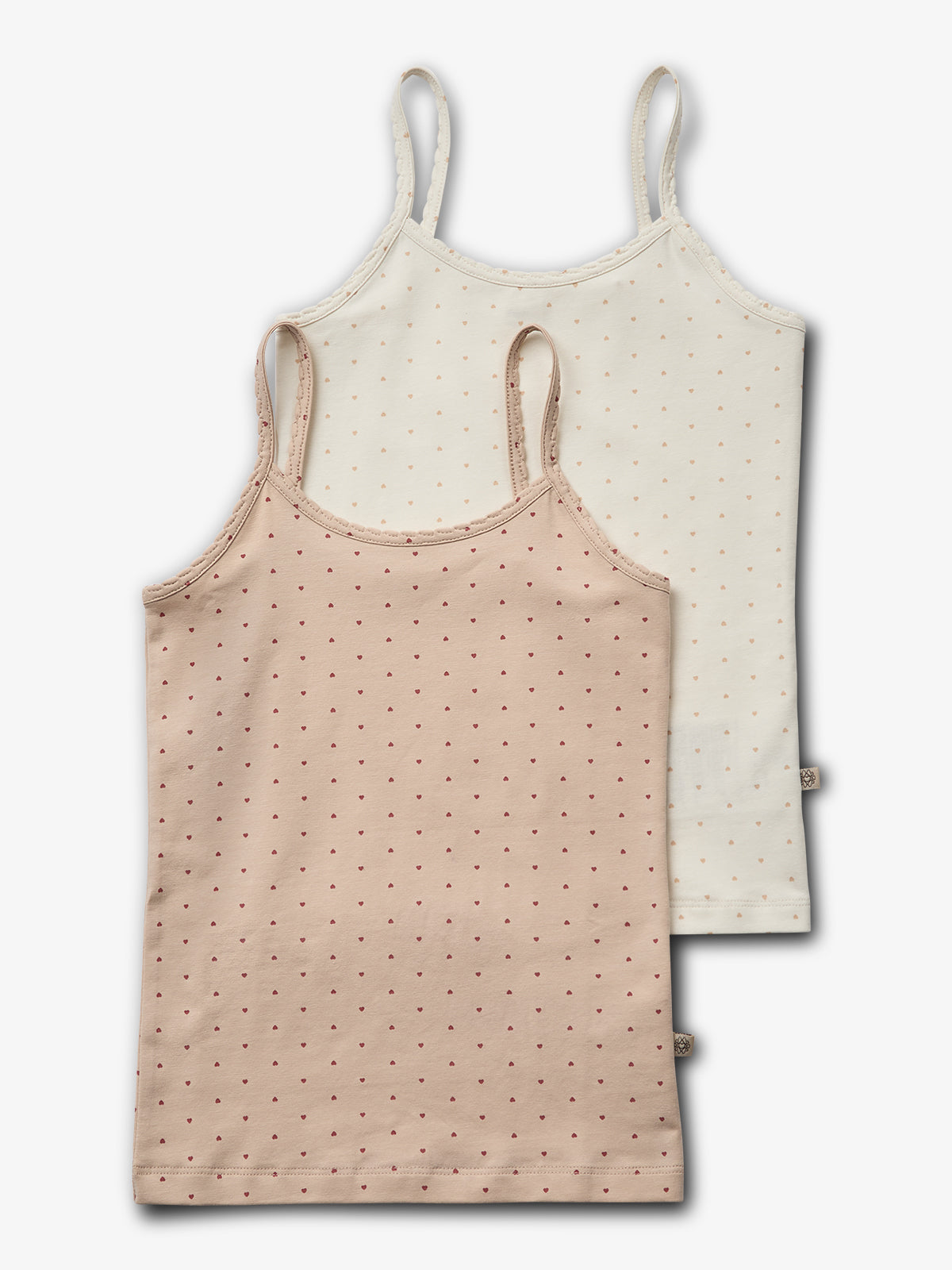 Twee hemdjes hangen overlappend. Het voorste hemdje is beige met kleine rode stippen, en het achterste is wit met vergelijkbare patronen. Beide hebben dunne schouderbandjes en zijn eenvoudig gestyled.