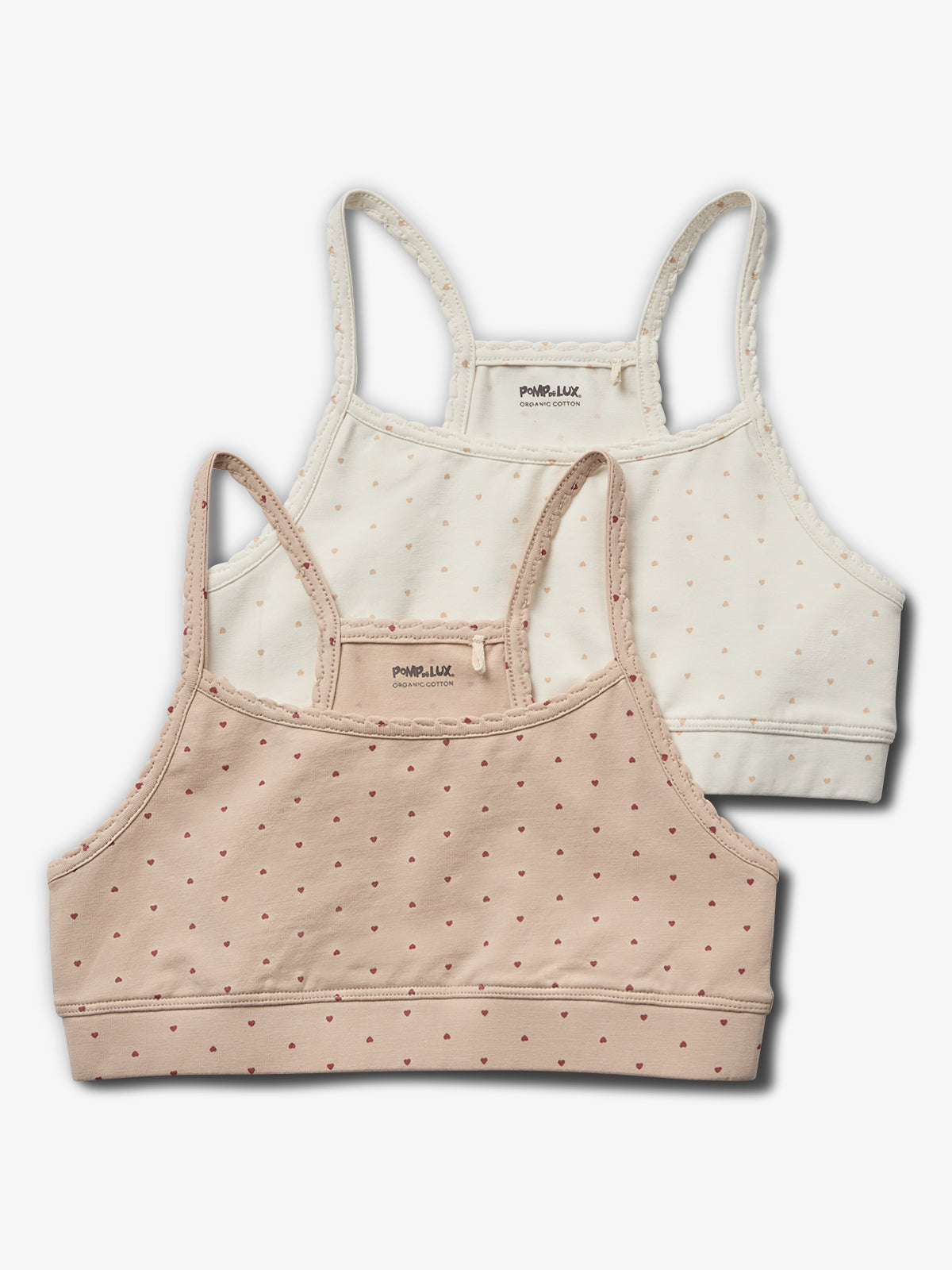 Twee gestippelde crop tops liggen gestapeld. De bovenste is crèmekleurig en de onderste roze. Beiden hebben dunne bandjes. De tekst "POMPdeLUX ORGANIC COTTON" staat erin.