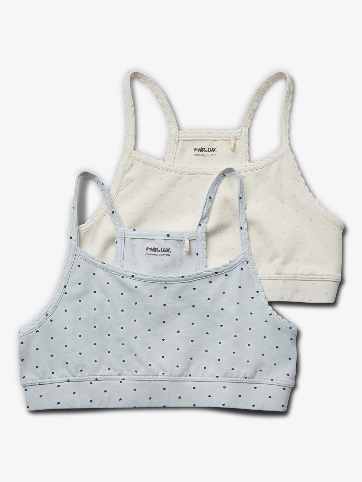 Twee kinderbeha's met smalle bandjes, één lichtblauw en één crème, beide met kleine hartjes. Tekst: "POMPdeLUX ORGANIC COTTON." Geïsoleerd op een witte achtergrond.